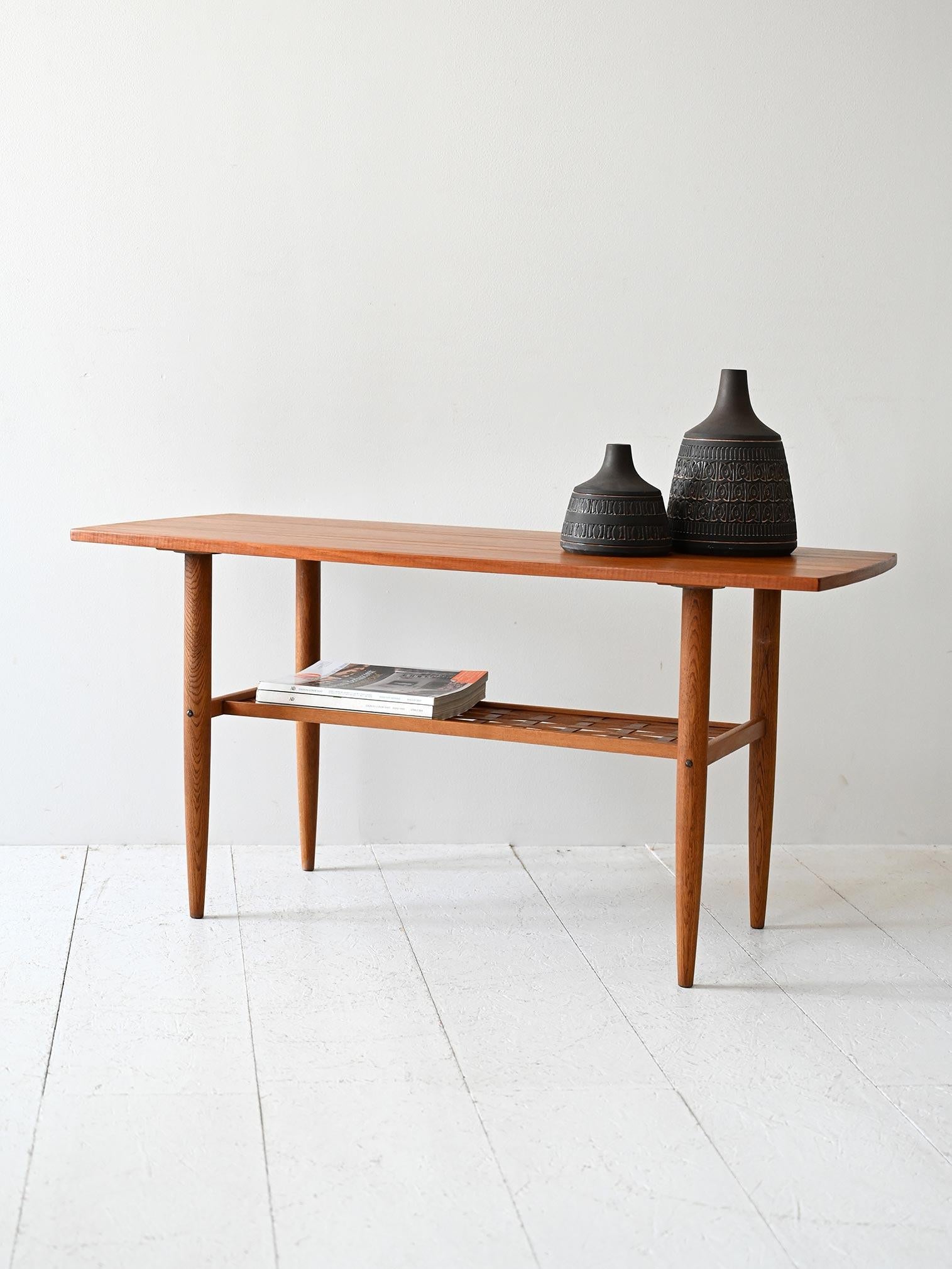 Tavolino in teak con gambe affusolate, piano smussato e ripiano intrecciato in fibra di legno a maglia ortogonale.

Tavolino da caffè scandinavo originale degli anni ’50/60, realizzato in teak con piano rettangolare dai bordi smussati. La struttura