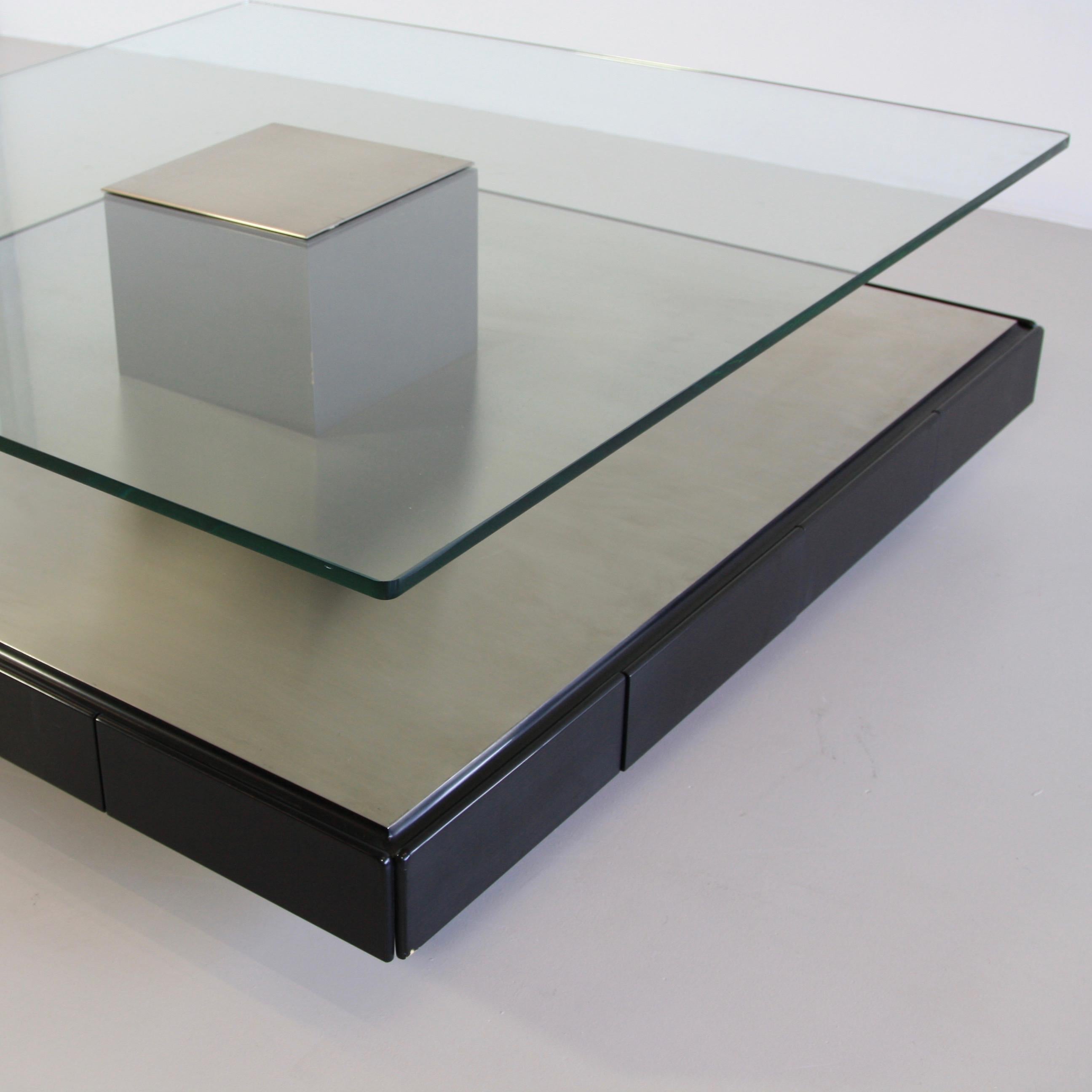 Large coffee table designed by Marco Fantoni. Italy, Tecno, 1971.

Minimalist coffee table (Tecno T147) with brushed metal base on wood containing eight drawers, thick glass shelf with brushed metal insert. Tecno labels on glass and all drawers.