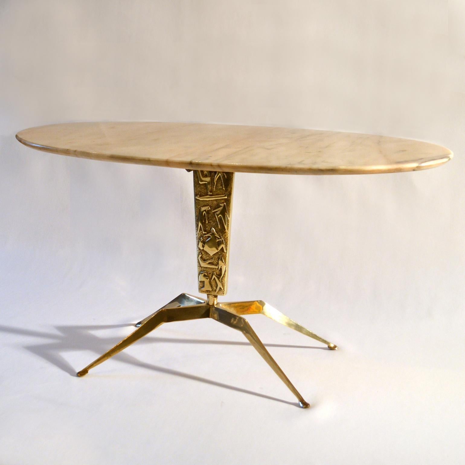 Oval coffee table with pink cream top with black veins supported by a sculpted cast brass base with a relief of figures and four spider legs on oval feet. The figures on the leg are abstracted in a typical 1950s style and tell the story of