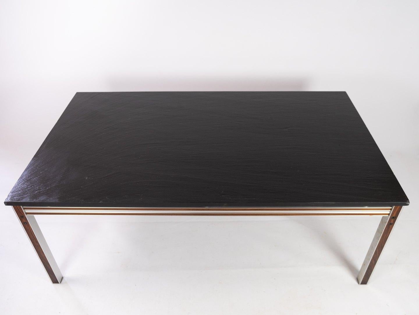 This coffee table epitomizes the sleek and modern aesthetic of Danish design from the 1970s. Crafted with a minimalist yet striking approach, it features a black slate plate elegantly juxtaposed against a frame crafted from rich rosewood and metal