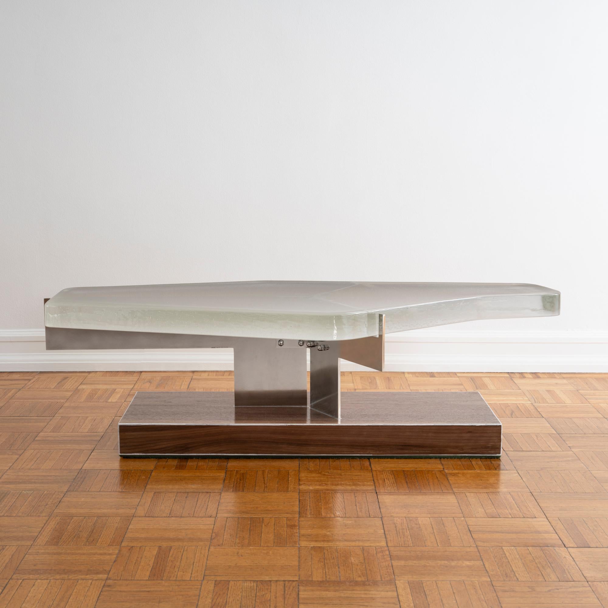 Unique, industrial and architectural coffee table composed of a cast glass slab top supported by cantilevered stainless steel atop a rectangular base in walnut veneered birch wood by London-based designer EJR Barnes. 

This piece creates a