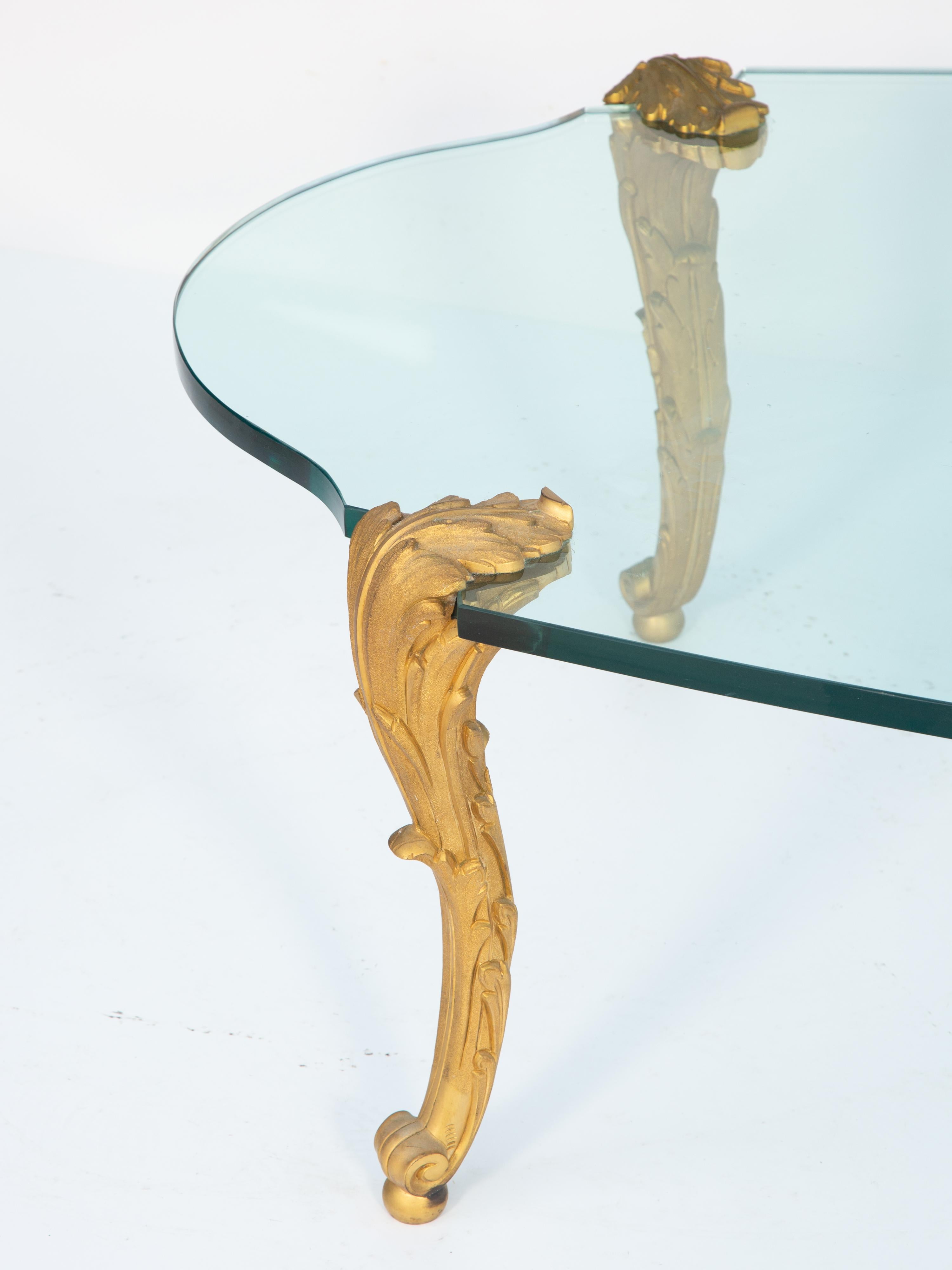 Table basse de forme classique par la fonderie new-yorkaise P.E. Guerin, à plateau en verre, reposant sur des pieds en acanthaine de style Louis XV, finement ciselés, en bronze doré, dont les parties supérieures se replient sur le plateau et se