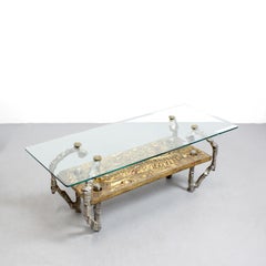 Mesa de centro con tapa de cristal, sostenida por una escultural estructura de metal fundido
