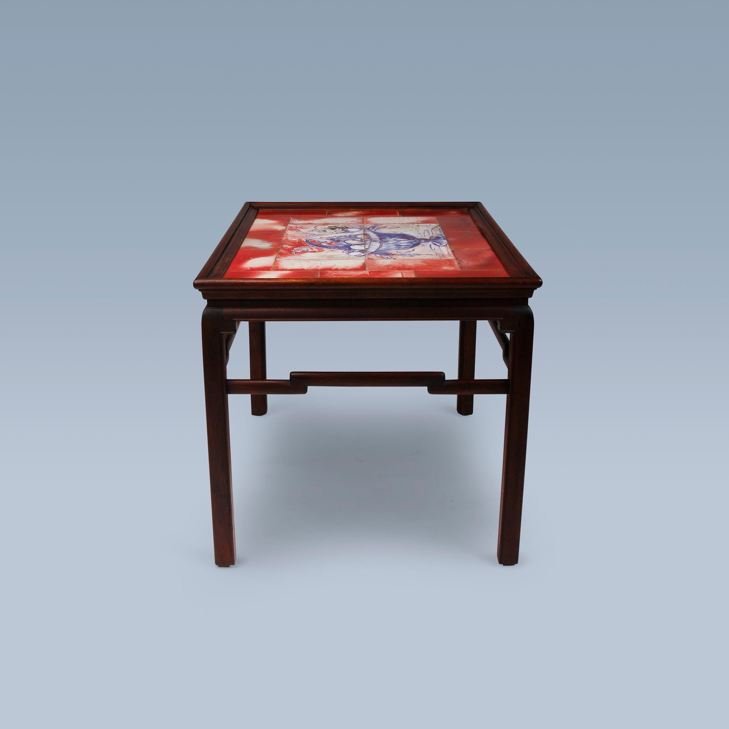 This so-called Chinese mahogany coffee table was executed by cabinetmaker Frits Henningsen ca. in the 1930s.

On top it has inlaid unique tiles depicting a fruit basket with decorative flowers. The tiles are handcoloured by painter and ceramist Jens