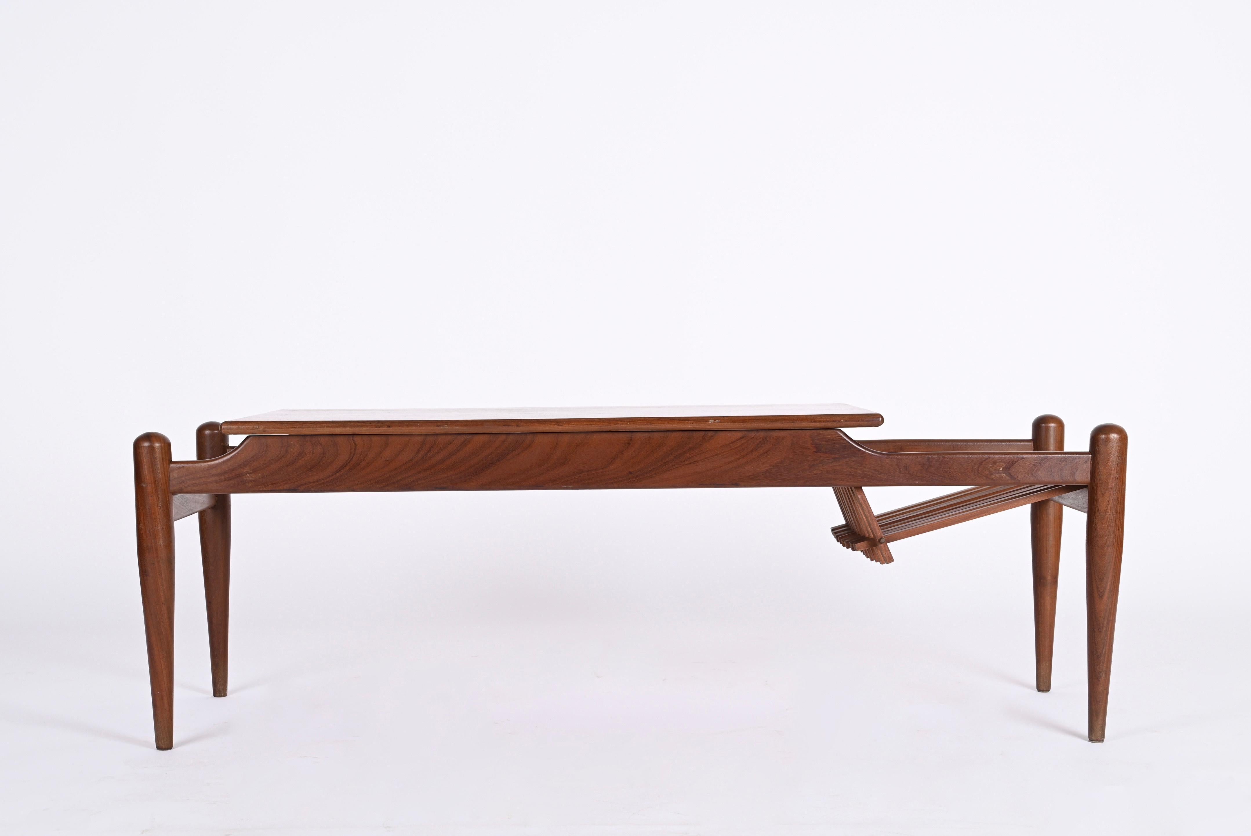 Superbe table basse avec porte-revues latéral en bois de teck. Produit en Italie dans les années 60 dans le style d'Ico Parisi.
Le grain du bois du plateau est tout simplement incroyable et la particularité de l'élégant porte-revues avec des