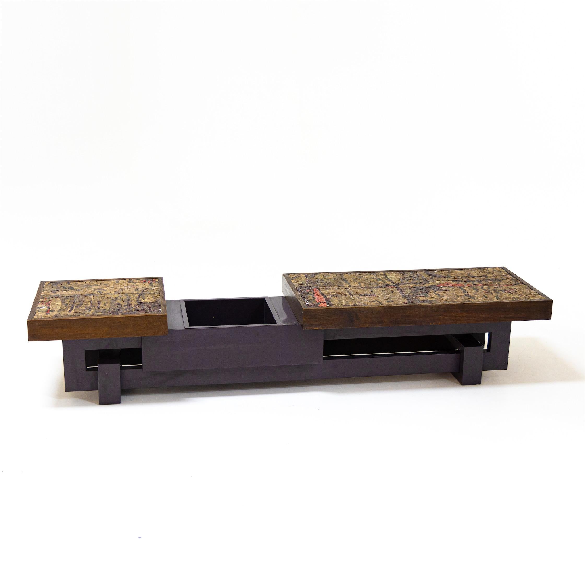 Long coffee table with stone mosaic and central plant bowl on a geometrically constructed, dark base.