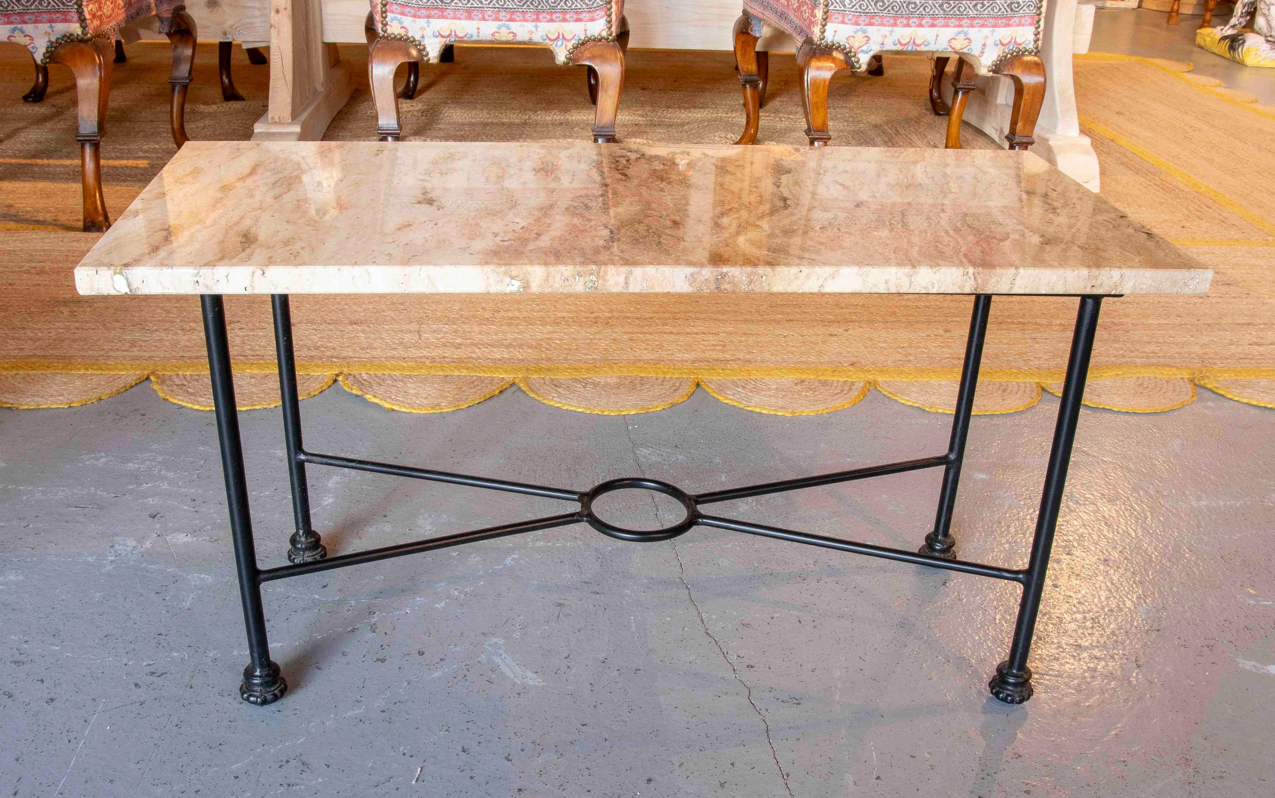 Elegante tavolino con piano rettangolare in marmo travertino beige con venature naturali che aggiungono consistenza e raffinatezza. La base è realizzata in ferro battuto nero, con un design lineare e un anello centrale come dettaglio decorativo,