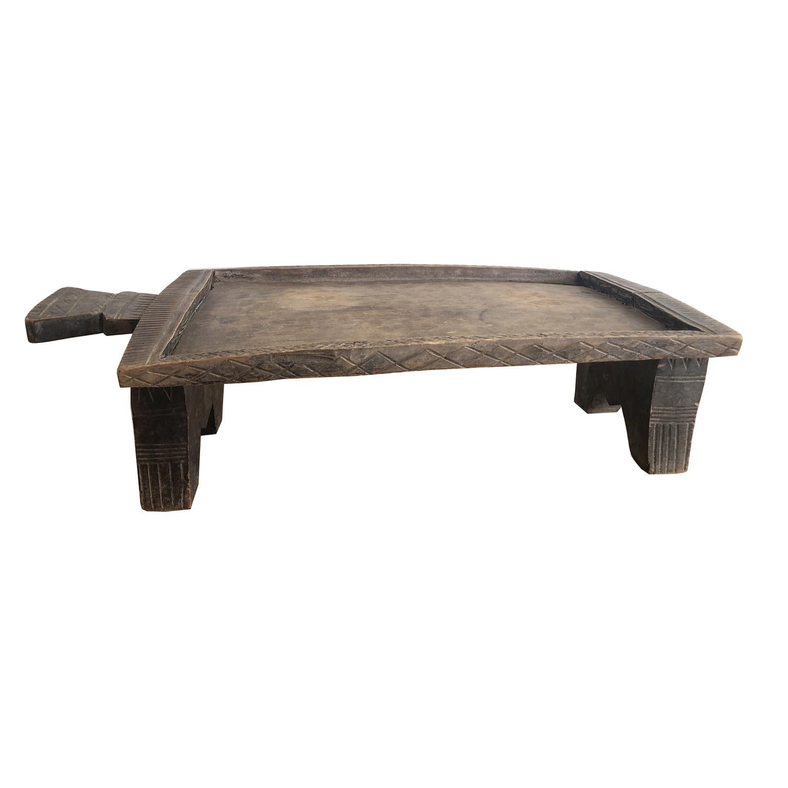 An Ethiopian coffee tray made from a solid piece of wood with rectangular top and handle resting on a trestle base from the Kaffa Province.  Incised geometric carvings embellish the borders of the top and stands, as well as the handle. This tray was