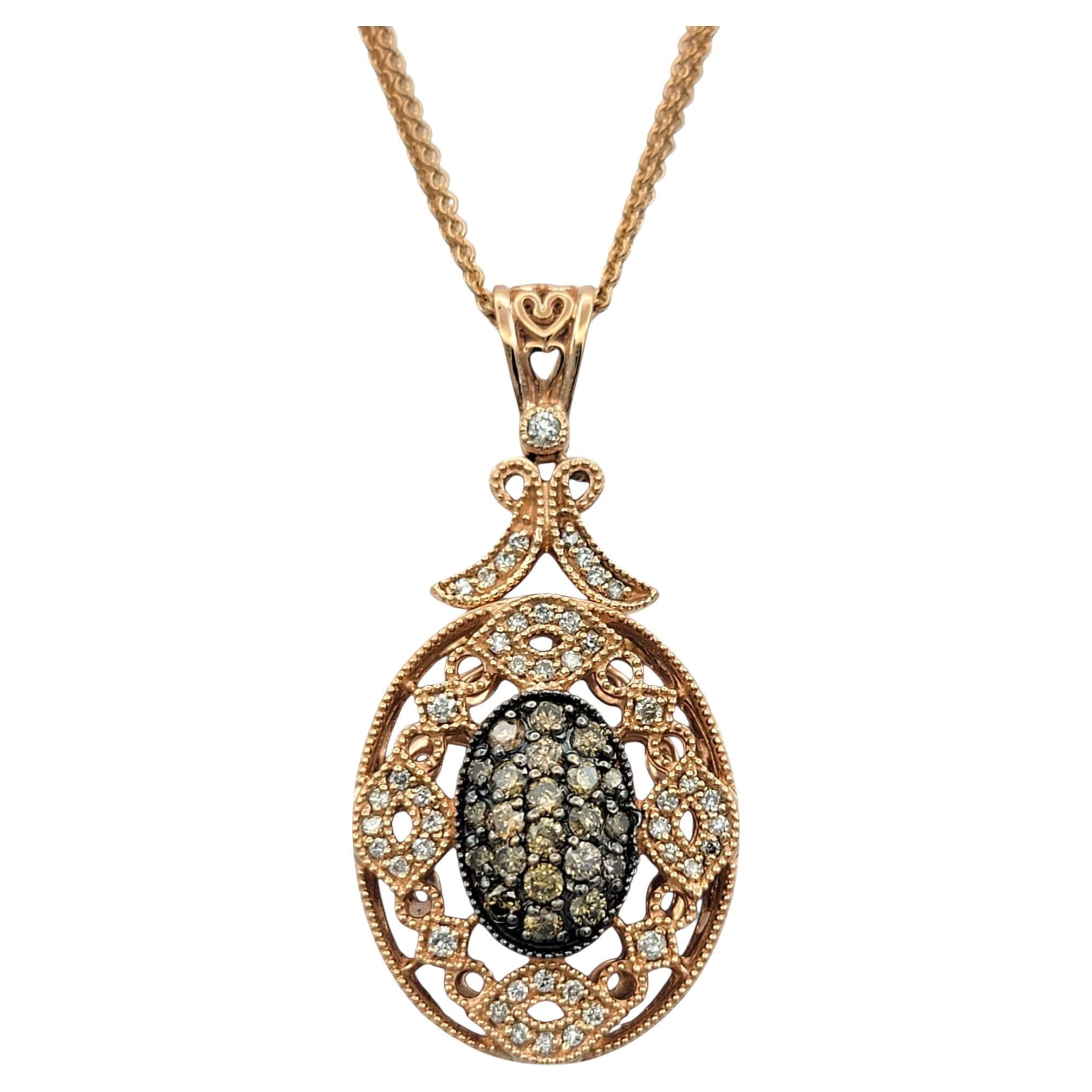 This intricate pendant necklace features a dramatic filigree design set in 14 karat rose gold, combining vintage charm with refined detail. At the heart of the pendant is a raised oval center, richly adorned with a mix of white and cognac diamonds