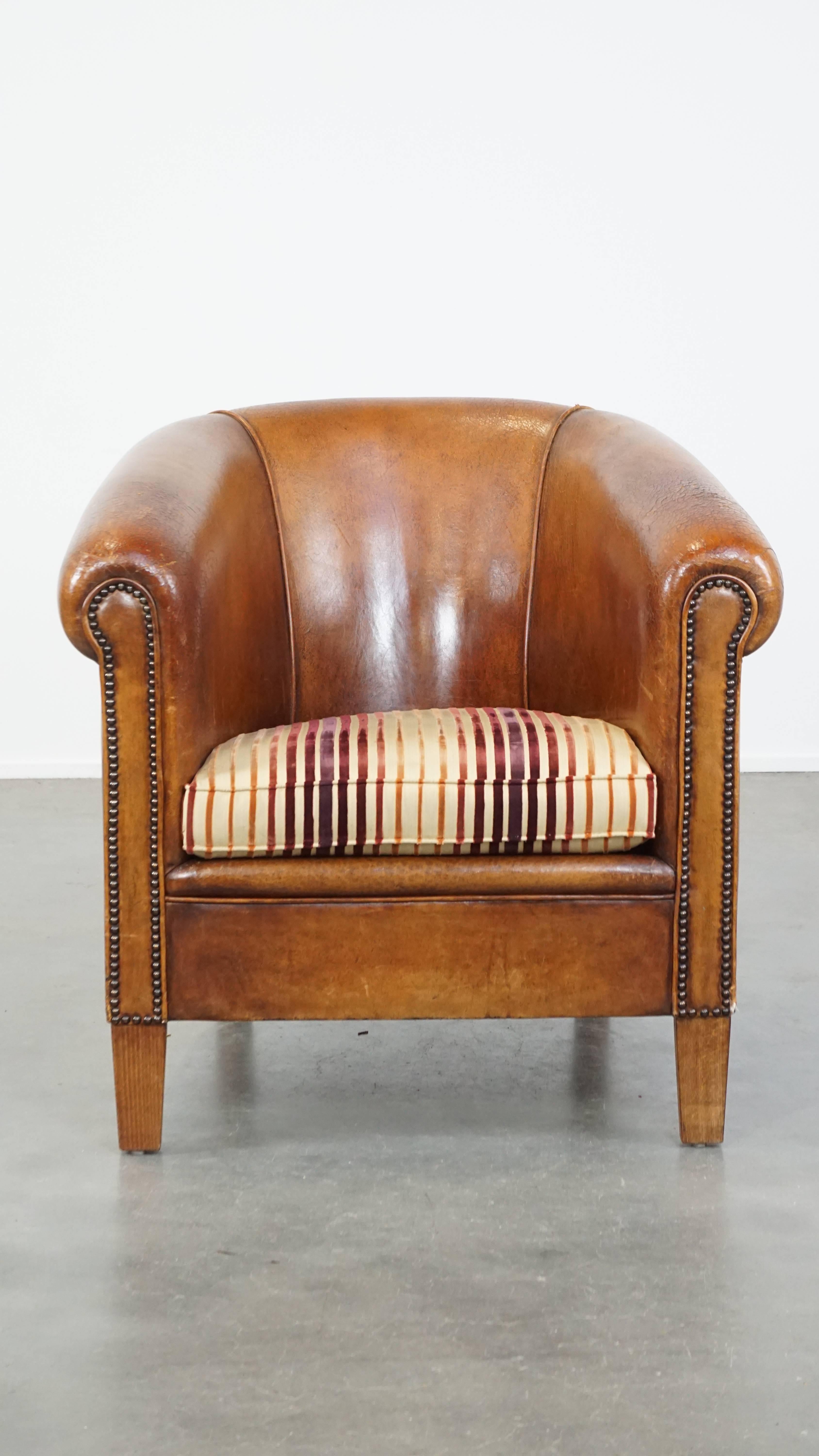 This stunning vintage sheepskin leather club chair is a true eye-catcher that deserves a place in any interior. With its warm cognac color and rich character, it exudes charm and elegance. The chair is beautifully finished with decorative nails and