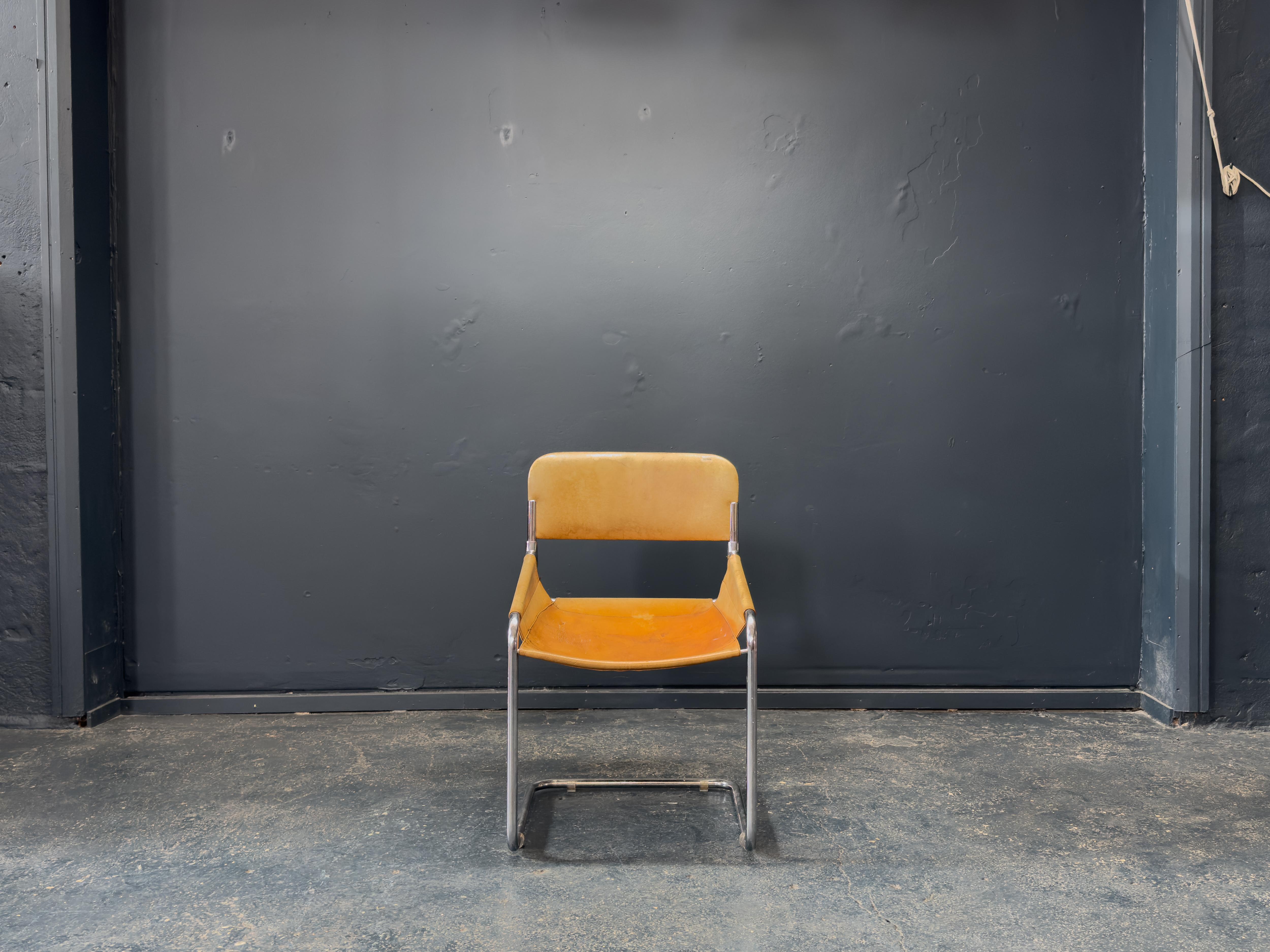 Esta silla tubular de cuero coñac y cromo es un sorprendente ejemplo de diseño modernista minimalista con una presencia claramente arquitectónica. La silla tiene un asiento y un respaldo flexibles, fabricados en piel coñac patinada que ofrece