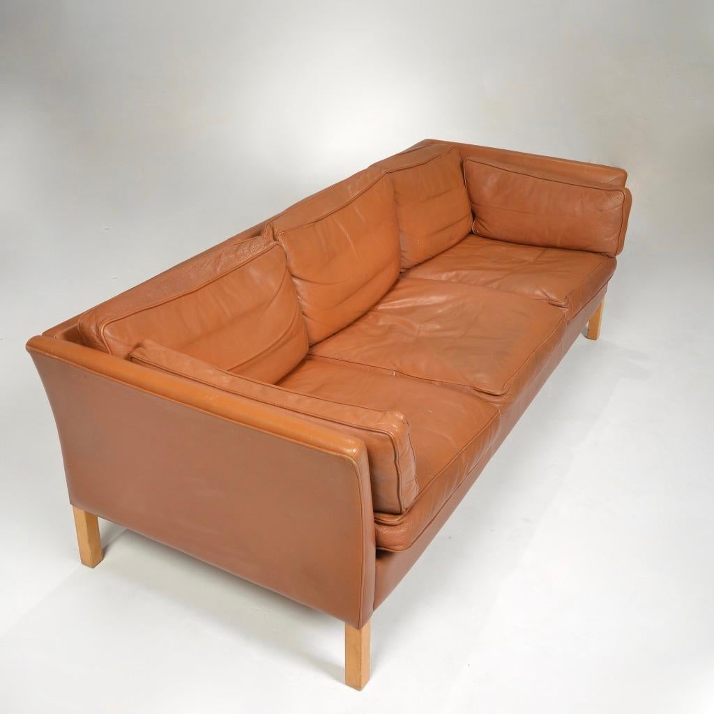 Three-seater sofa designed by Hans Olsen in cognac leather with wooden legs.
Leather has a beautiful patina.
  
