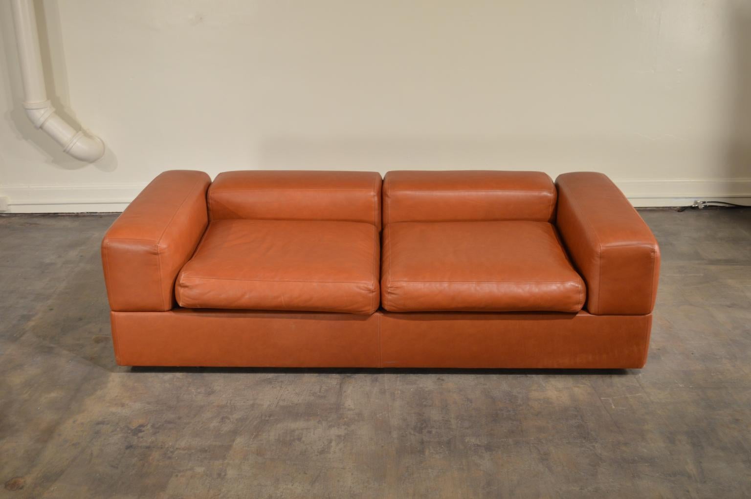 Cognac leather sofa daybed designed by Tito Agnoli for Cinova of Italy. Levered arms and back conceal laminate shelves on the underside that can be used as shelves. The seat cushions rest on a springed mattress underneath. Mattress can be removed
