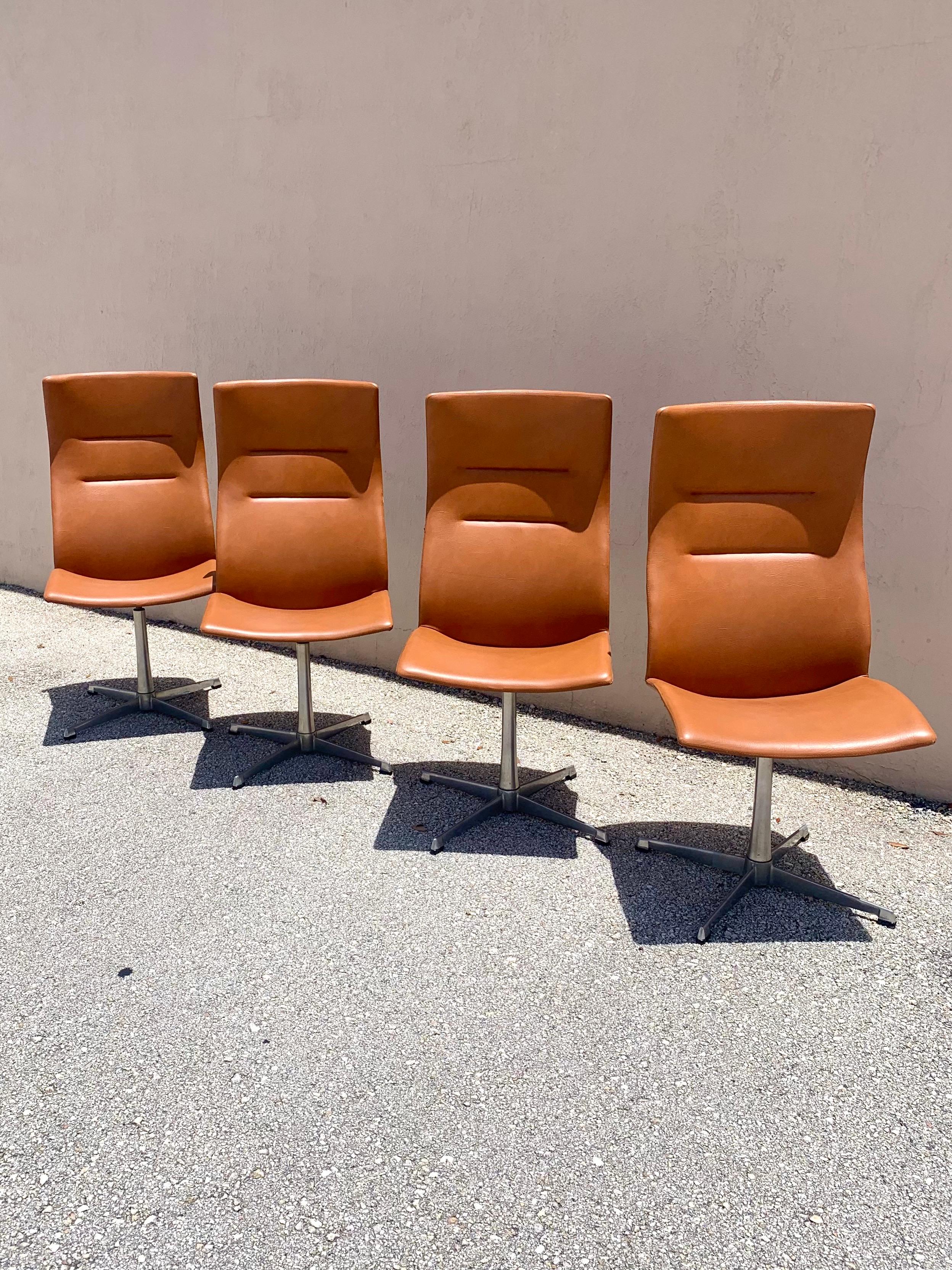Tolles Set aus 4 Esszimmerstühlen von Overman. Hergestellt in Schweden. Hohe ergonomisch geformte Rückenlehnen, die von einem 4-Stern-Drehfuß aus Aluminium getragen werden. Cognacfarbenes, hochwertiges Vinyl. Sehr bequeme und stützende Sitze.
