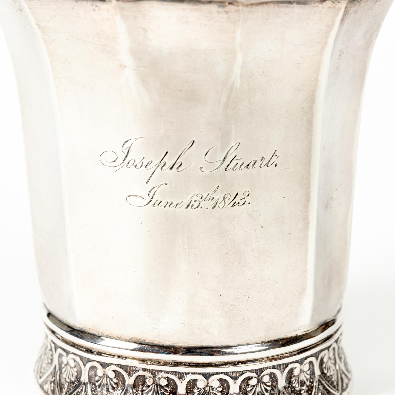 Circa mid-19th century coin silver mug with s-scroll shaped handle, engraved with the name Joseph Stuart and the date June 13th 1843. This early coin silver mug was tested, not marked. The bottom of the cup is also decorated with reliefs of heart