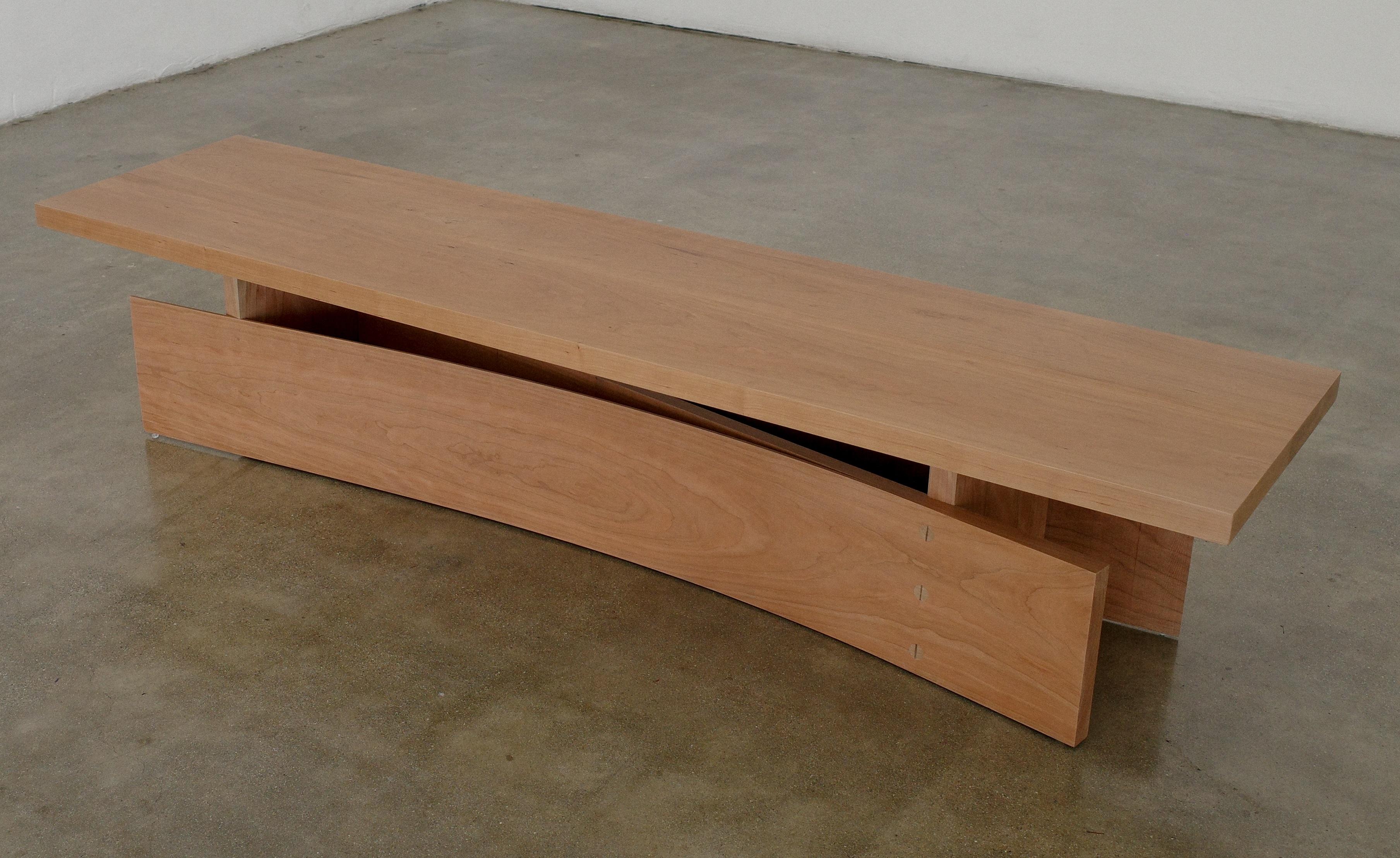 Cold bent bench by Nick Pourfard.
Dimensions: D 56 x W 213.5 x H 43 cm.
Materials: wood.
Different finishes available. 

Wood is bent without steam or lamination, playing advantage to tension and memory built into the wood