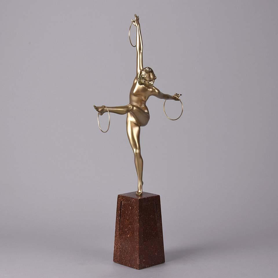 An energetic Art Deco cold painted bronze figure of a naked dancer balancing a set of three rings on her hands and outstretched foot. The surface of the bronze with good deep golden colour, the figure raised on a shaped marble base the top of which