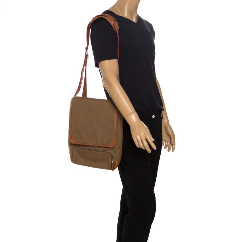This Cole Haan messenger bag is stylish and functional. Crafted from brown canvas, it comes with leather trims. It is equipped with an exterior pocket, a shoulder strap, a flap that opens to a fabric interior with enough space for essentials. It is
