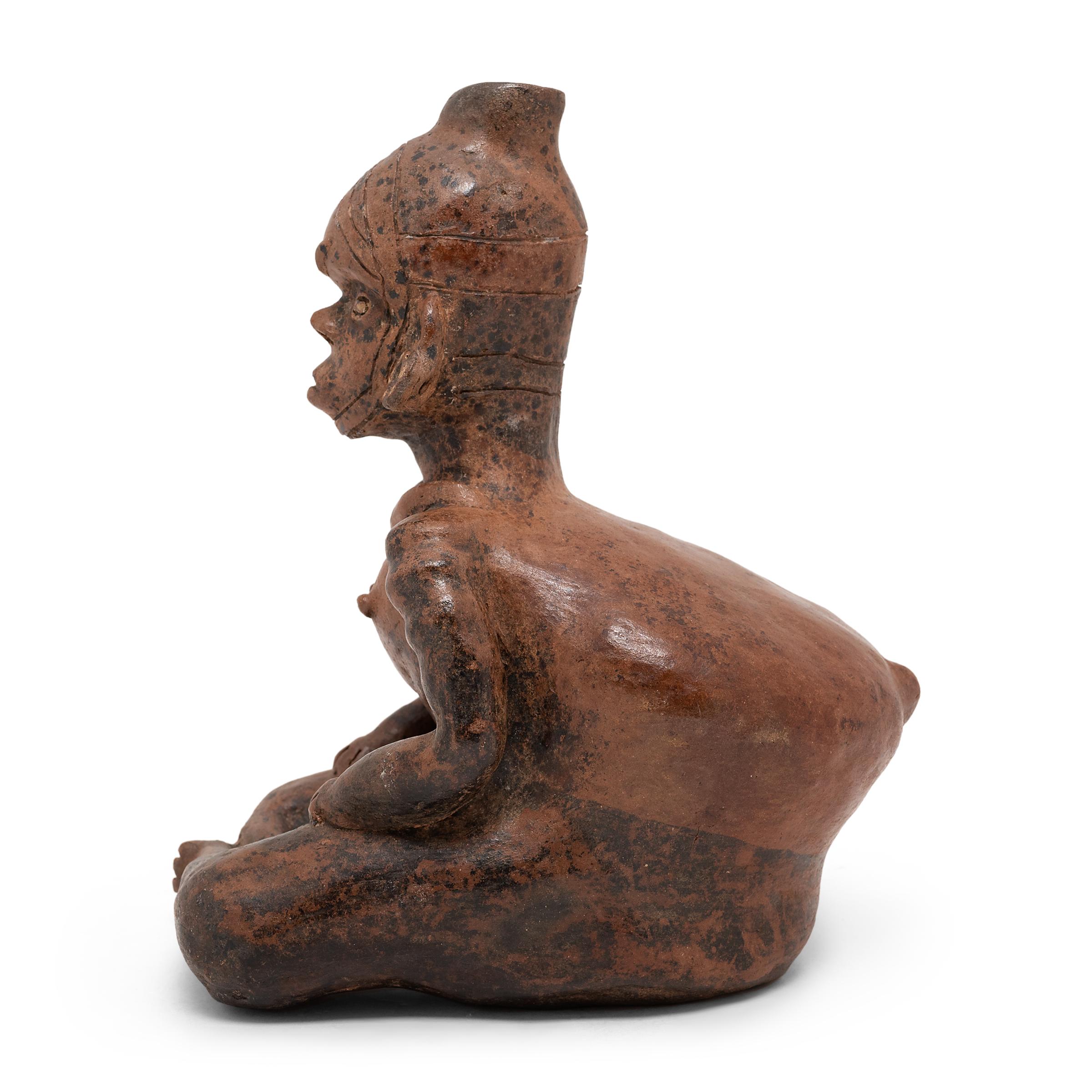 Beautifully aged with a rich patina and pitted wear, this seated ceramic male figure is attributed to the Colima region of Western Mexico. The stylized form of this male figure follows the conventions of Colima pottery, emphasizing squat bodily