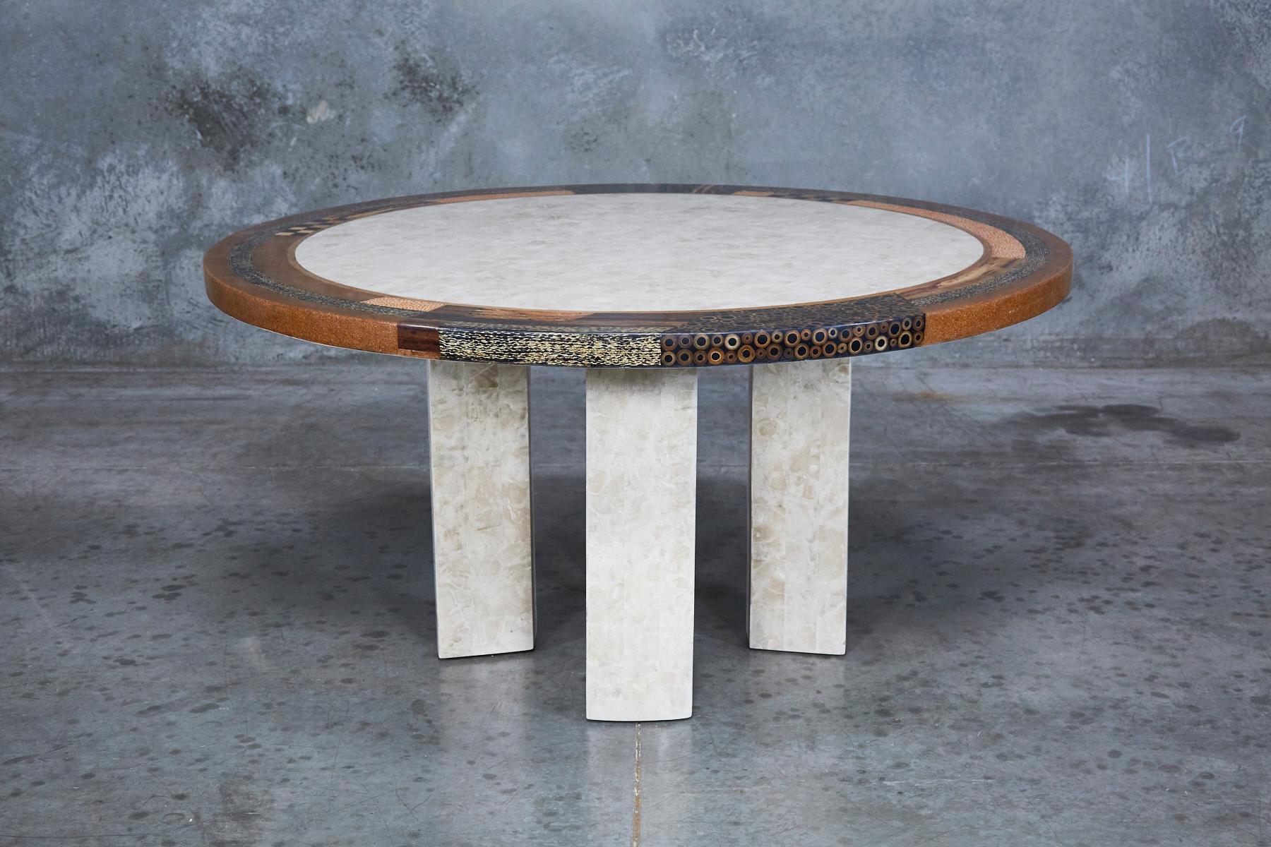 Round dining table with rectangular columnar legs and 60 in. diameter top, both in tessellated stone. Tabletop with decorative edging featuring inlaid exotic natural materials including bamboo, cotton husks, honeycomb cane leaf, corn tassel, and