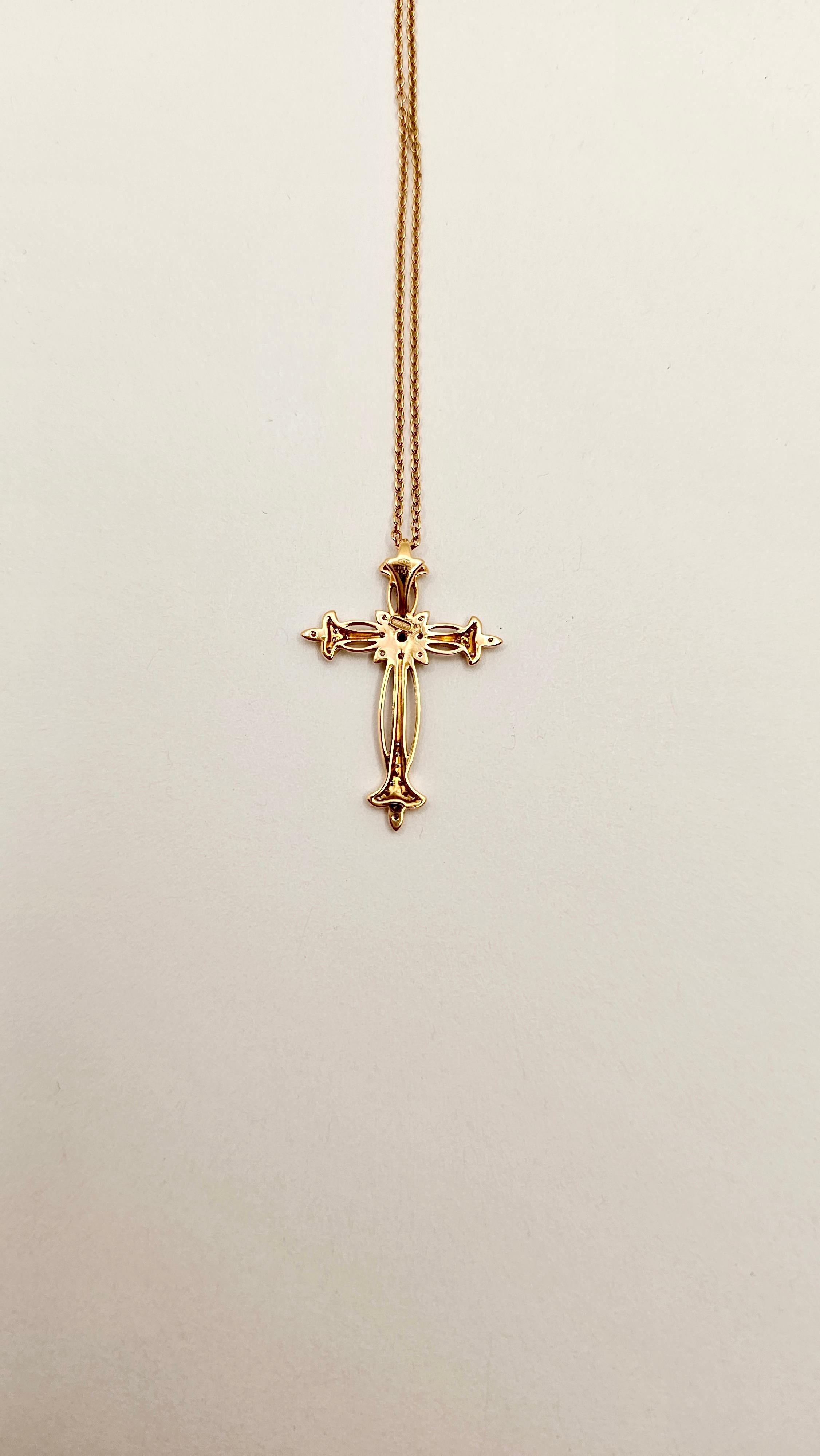 Un collier en or rose 18 carats avec pendentif en forme de croix, dans le style gotique, orné de diamants.
Le pendentif est orné d'une peinture à l'or fin et de micro-pointes. Au centre du pendentif se trouve un motif floral avec des diamants