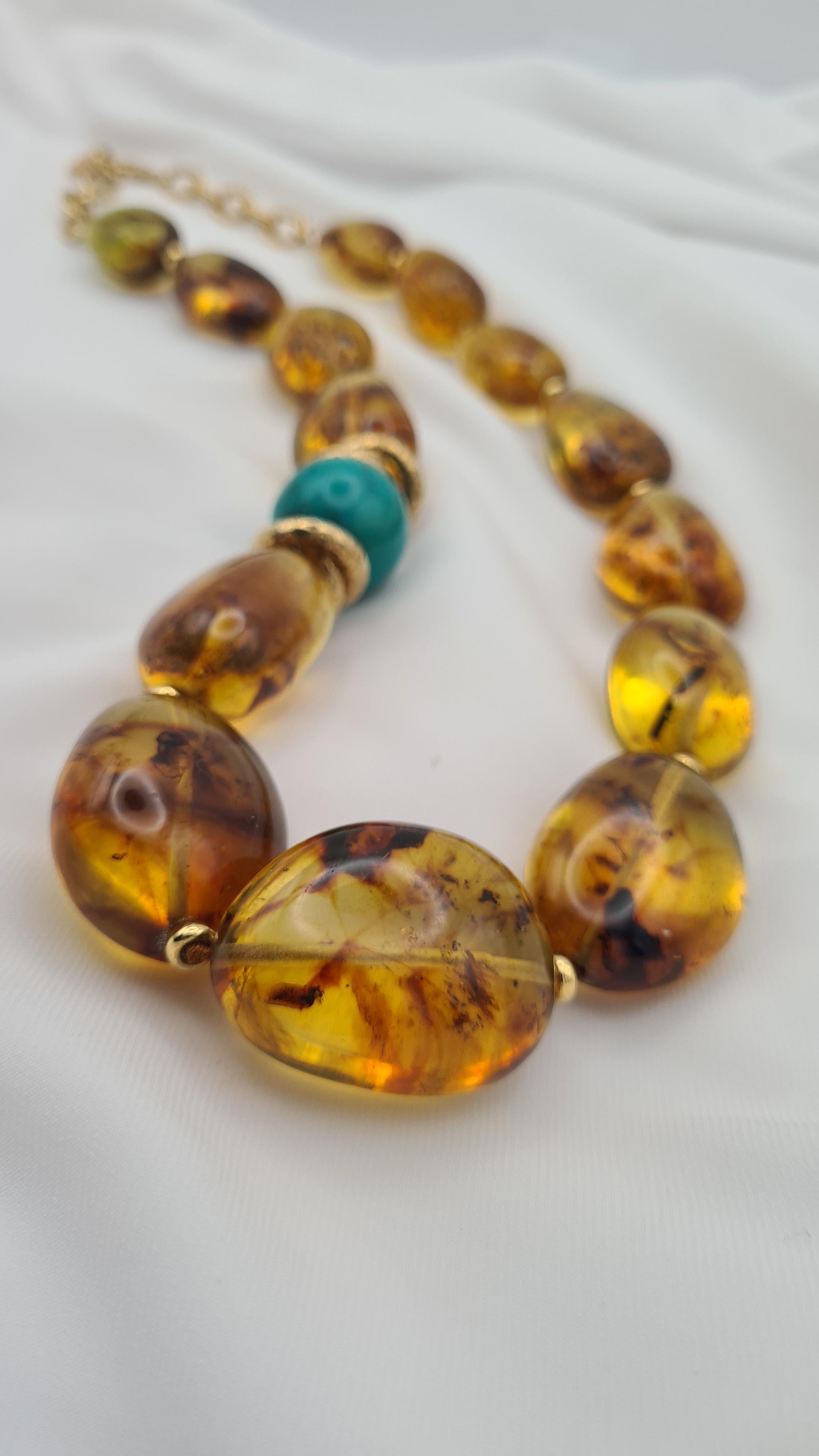 Collar con grandes elementos regulares de ámbar báltico de color coñac. Los bellos elementos de ámbar en escamas están adornados con motivos de Plata925 martillada y chapada en oro de 24 quilates; estos últimos rodean una esfera de Turquesa,