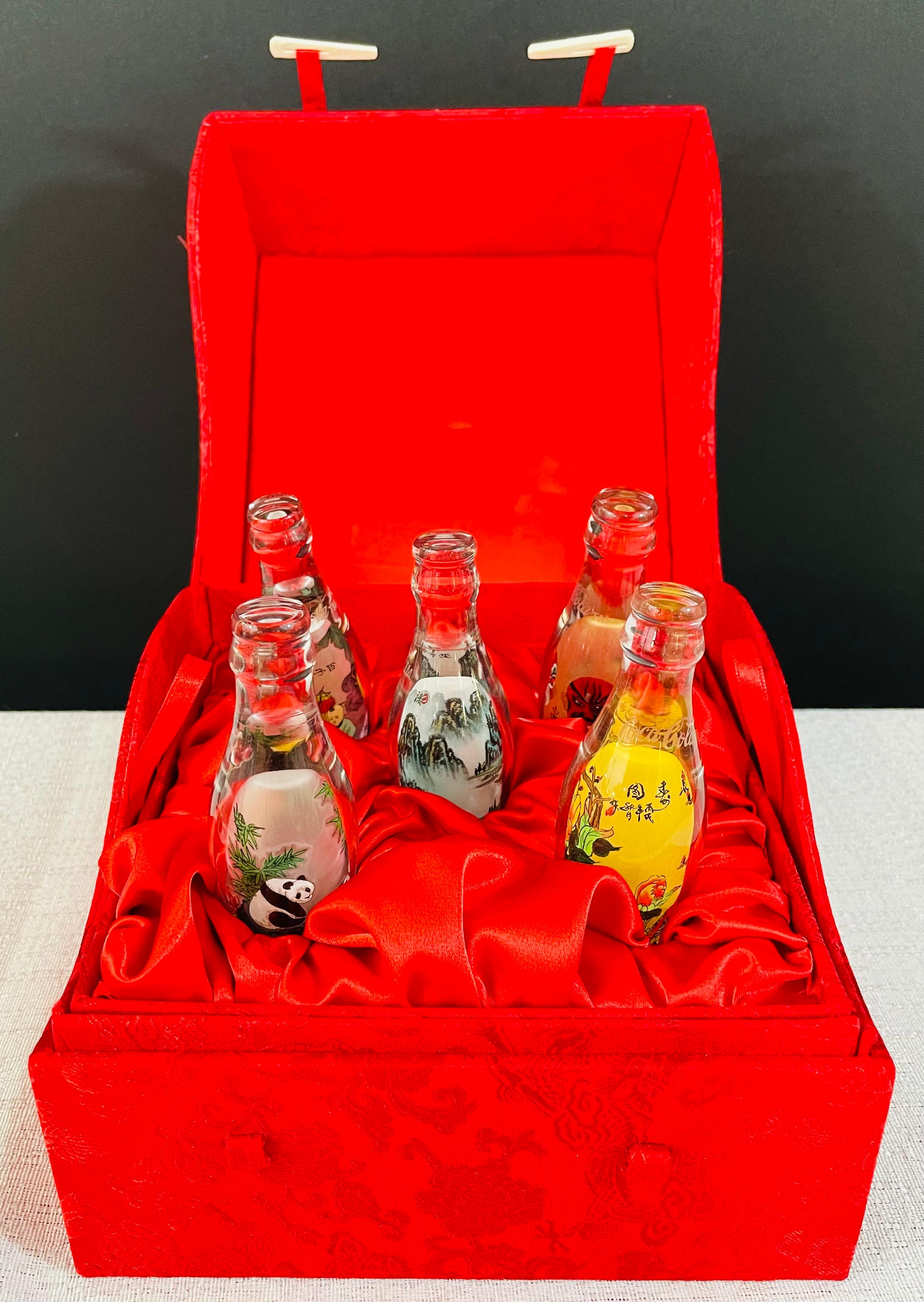 A custom made special edition Coca-Cola set of 5 miniature glass bottles. Each bottle is handprinted to portray traditional Chinese emblems such as masks, floral and figural design, panda as well as landscape. The bottles are raised on a round hand