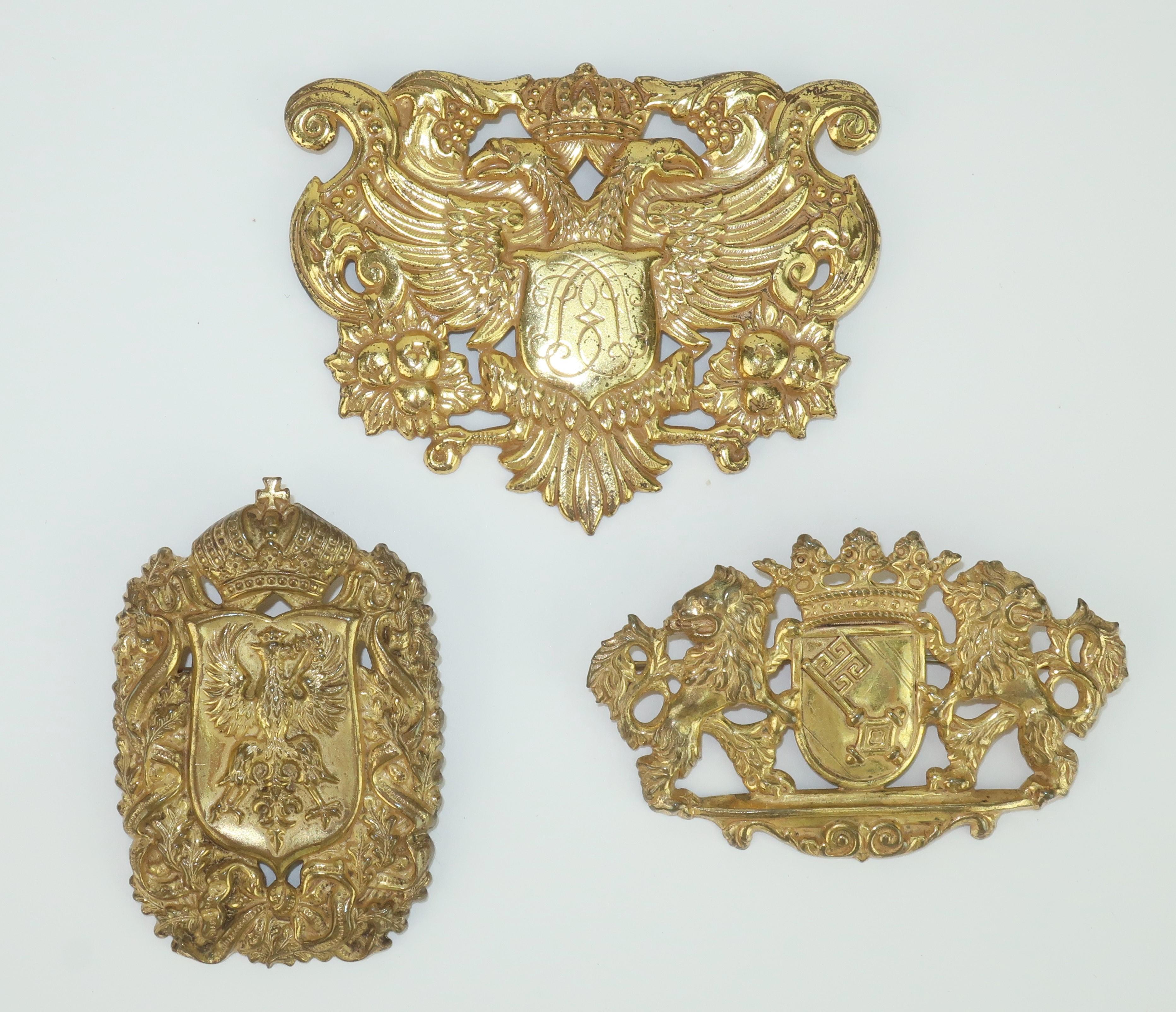 Collection of three 1950's Miriam Haskell medallion coat-of-arms brooches in a gilded metal with Victorian era details.  Each brooch appears to replicate a classic European coat-of-arms including lions, phoenix and eagle.  Outfitted with straight