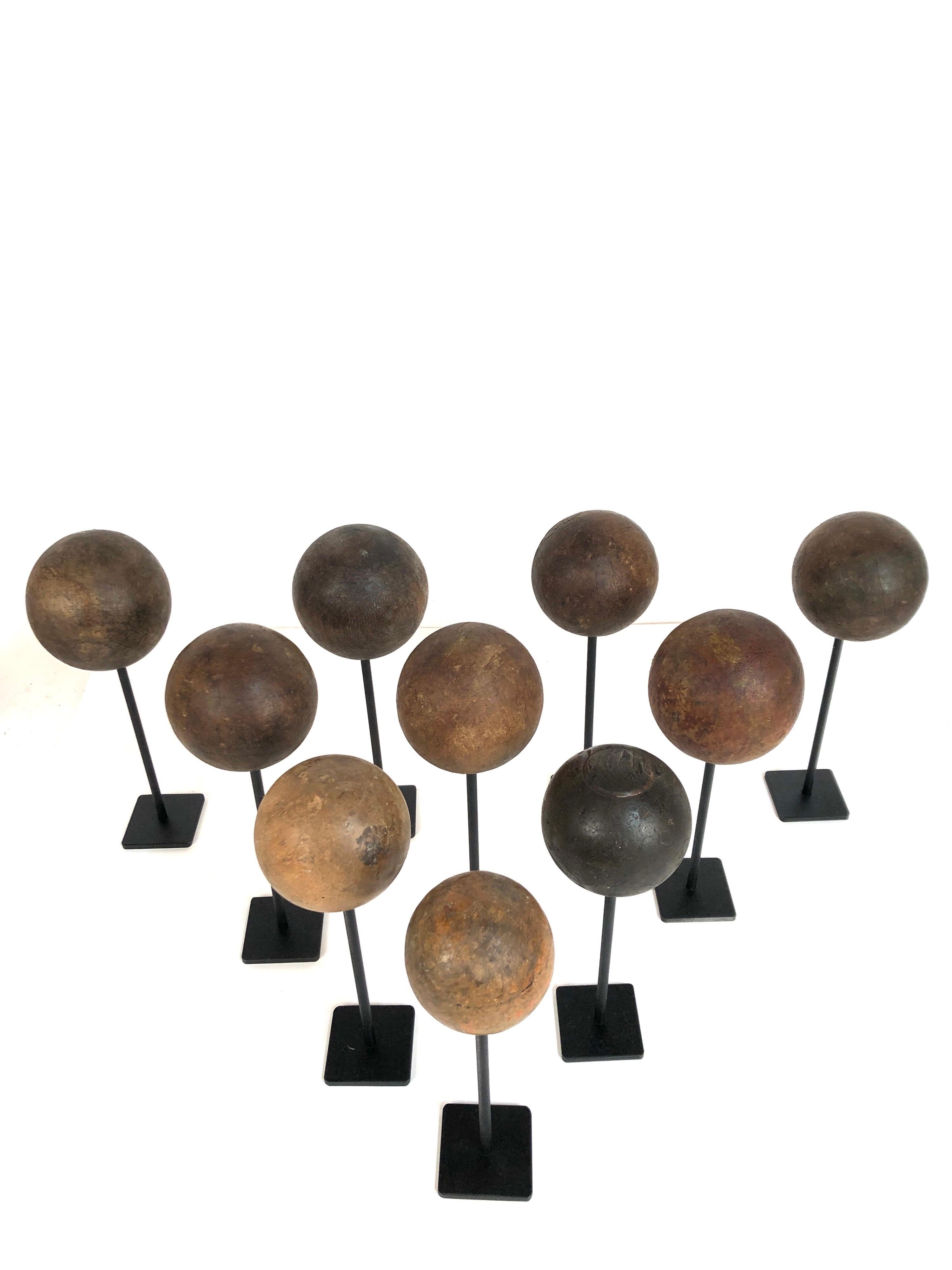 A collection of 10 antique wooden balls. All from various games including bocce and croquet. Varying colors and woods. All waxed and custom mounted on black painted steel stands. They range in size from 9