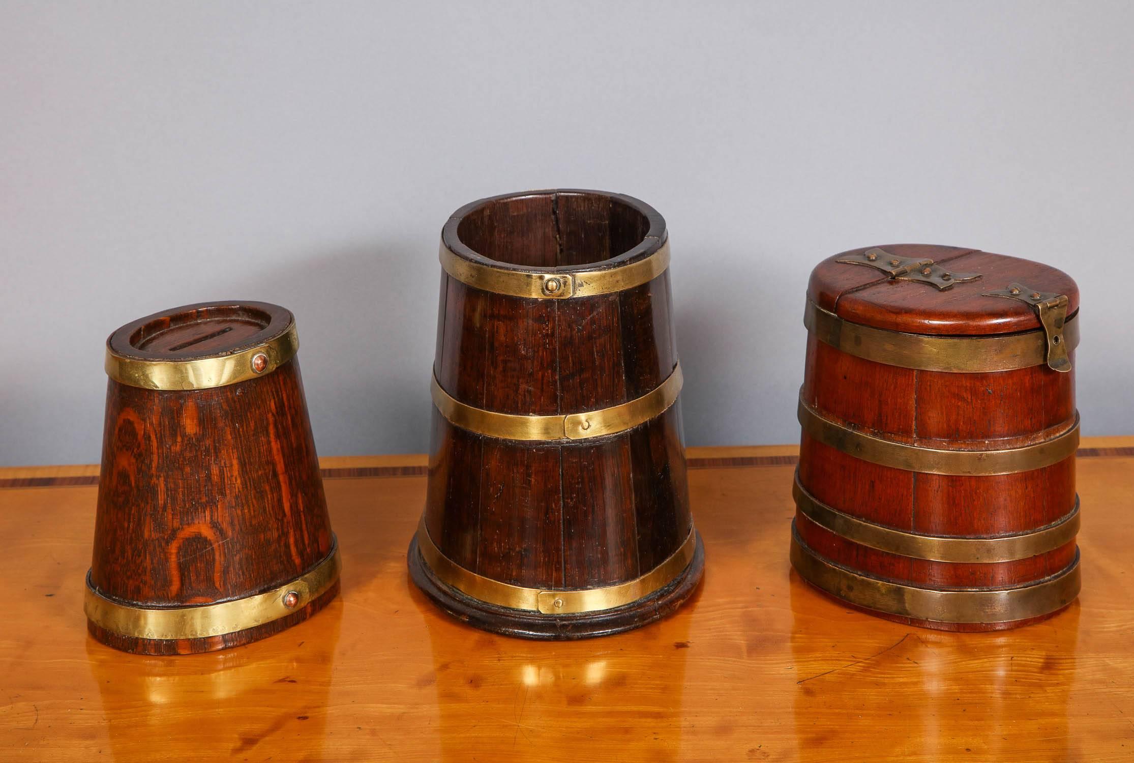 Lovely collection of three English 19th century brass bound staved vessels all of oval flaring form, the first (with two bands) an oak money bank in the form of a ship's tobacco barrel, the second (three bands) an early 19th Century Georgian
