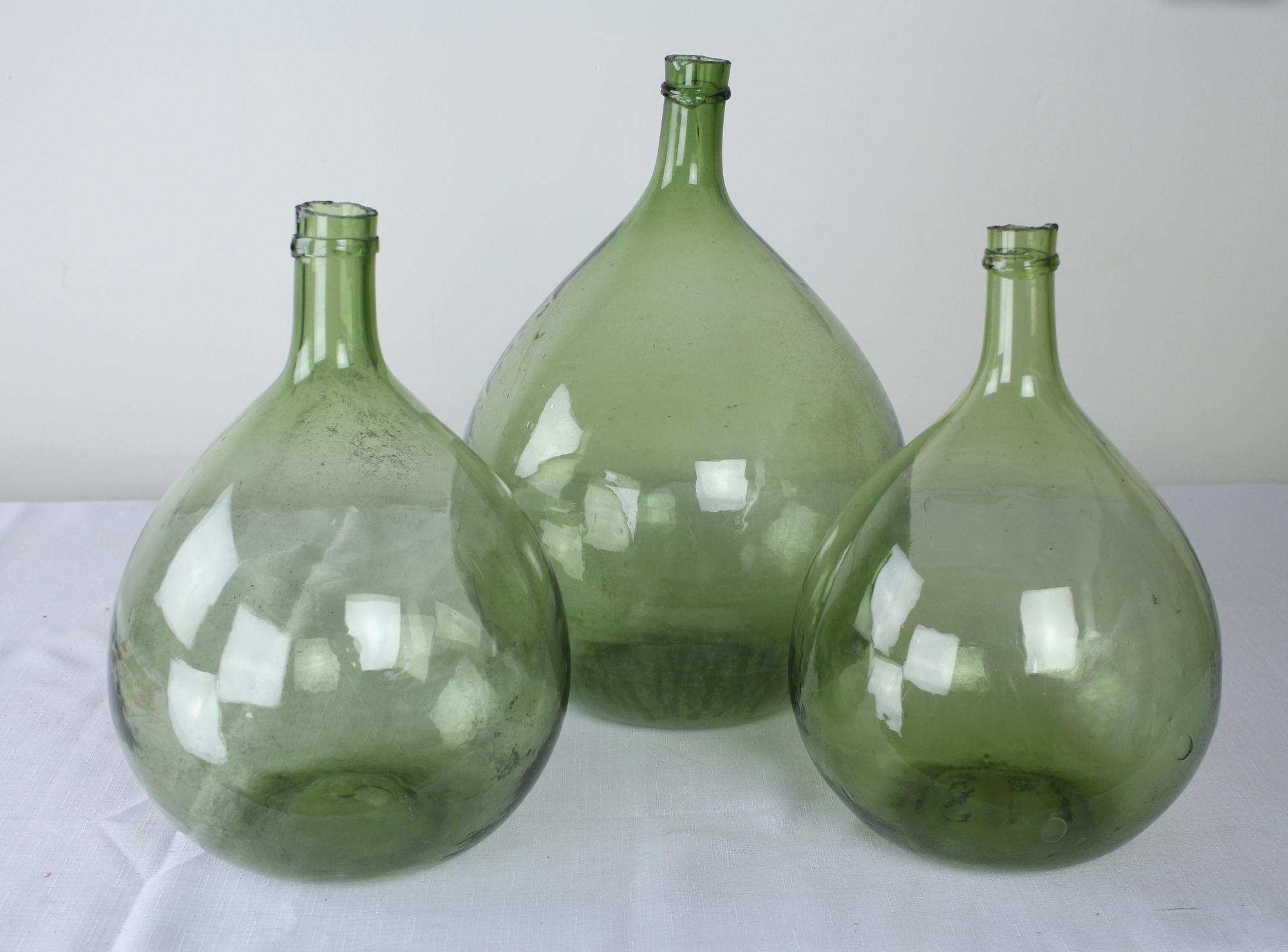 A collection of three olive colored glass demijohn bottles, used from the late 17th Century through the 19th Century to carry wine and spirits. Handblown, each has their own unique characteristics, from the tilt of the gooseneck to the trapped air