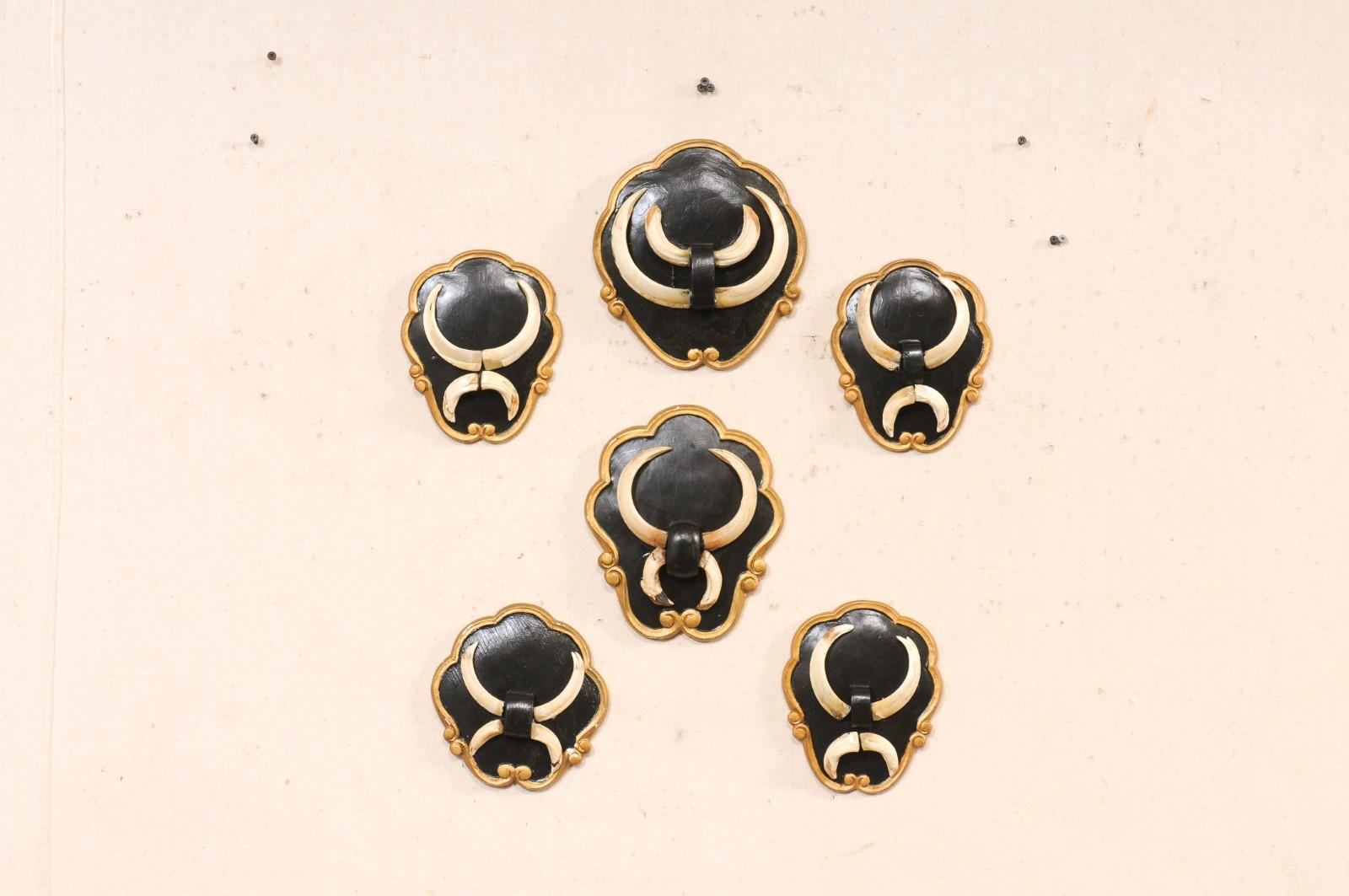 A collection of six European wall plaques with mounted boar tusks from the mid 20th century. These vintage wall decorations from Europe each have a slightly varying shape and size, but overall they have been designed with a frame comprised of