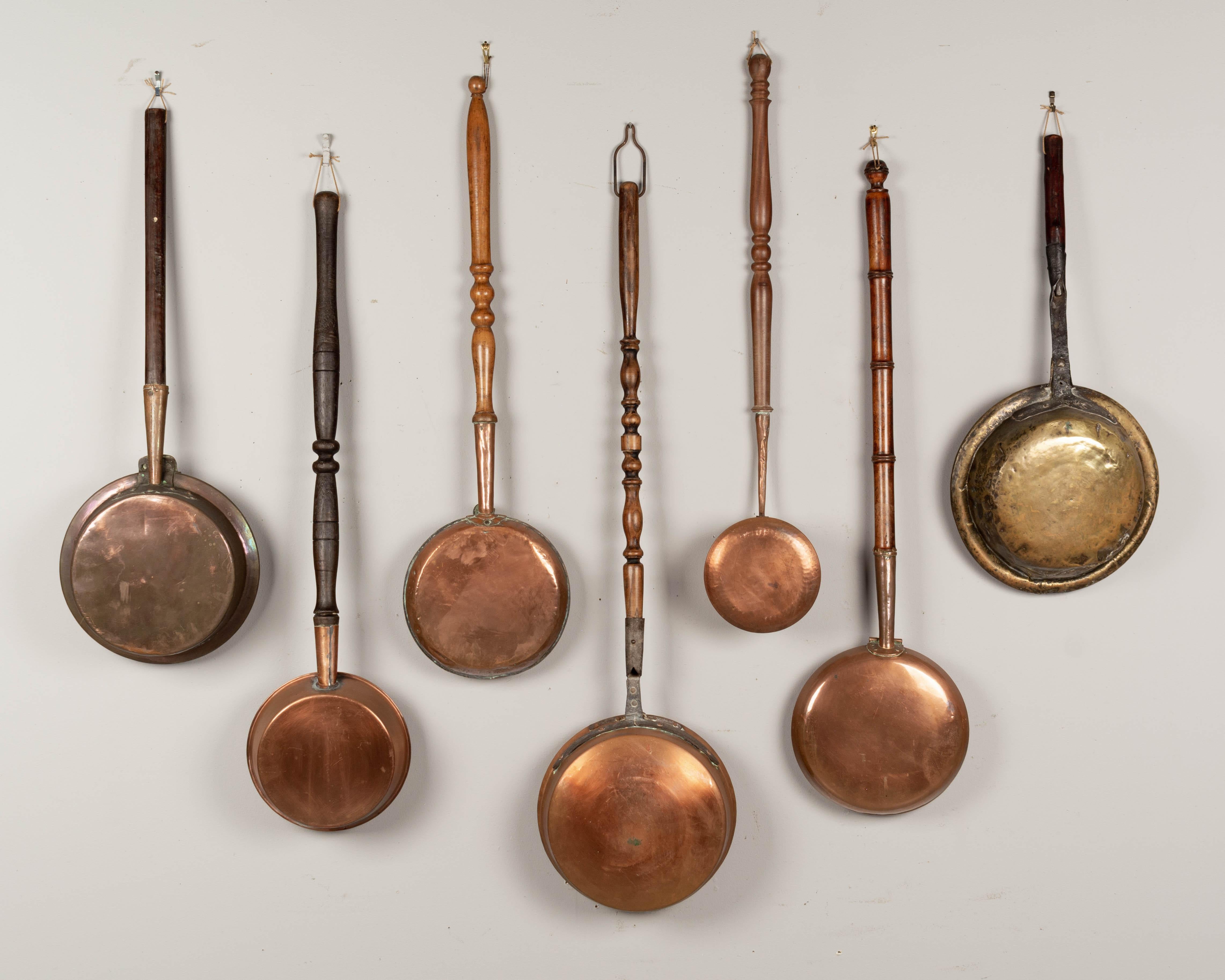 A collection of seven French bassinoires, or bed warmers, ranging in age from the 18th century to the early 1900s. Six are copper and one brass. All with hinged perforated lids and turned wood handles. The one on the right is from the 18th century