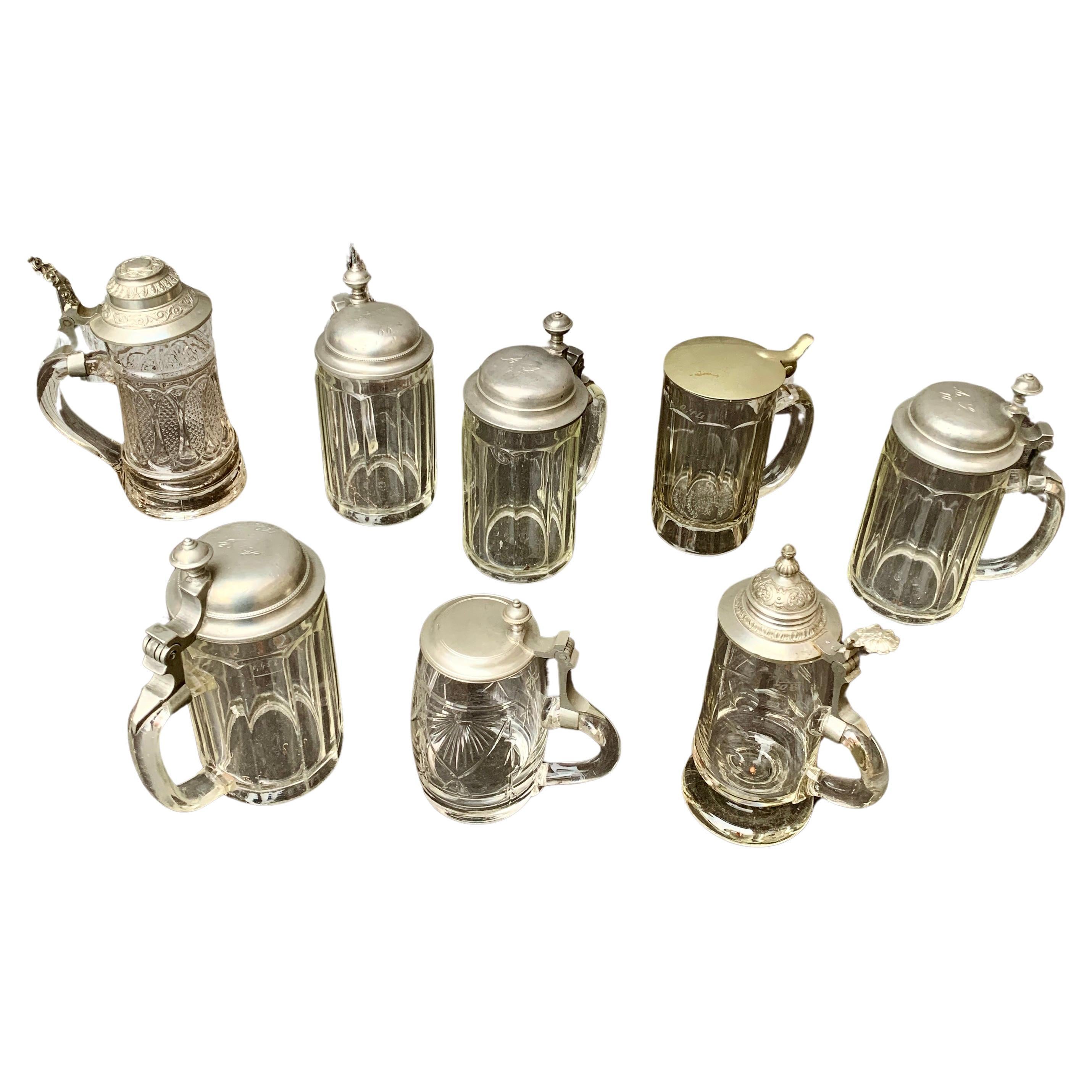 Une collection de 8 pièces de choppes en verre avec couvercles en métal de la fin du 19ème siècle et du début du 20ème siècle. Ils ont probablement été utilisés pour boire de la bière. Quatre d'entre elles du même modèle ont un numéro imprimé dans