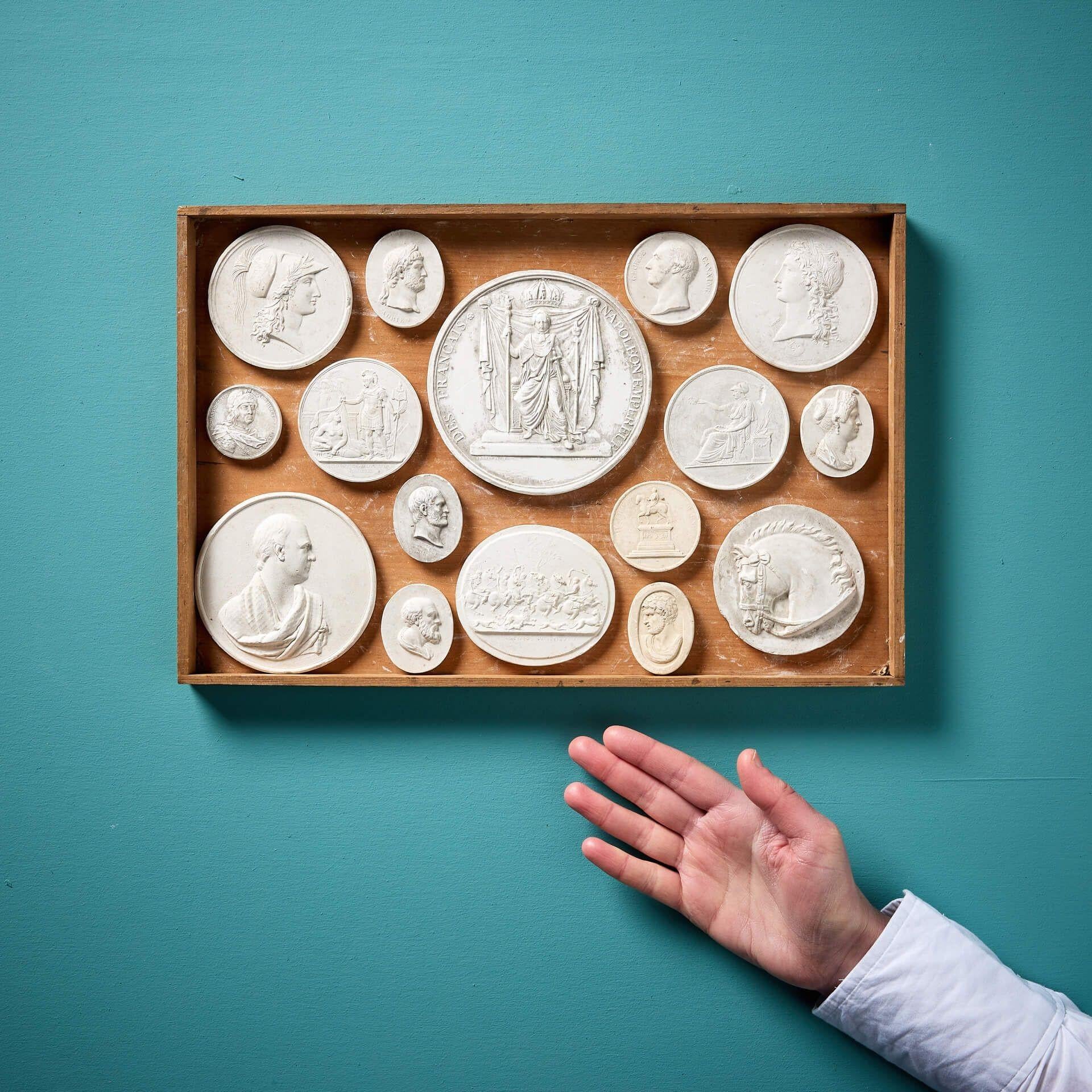 A superb collection of 16 antique plaster cameos and intaglios of French and English origin presented in a wooden tray, supplied loose. These 19th century plaster cameos each display a neoclassical style relief decoration across roundels and oval