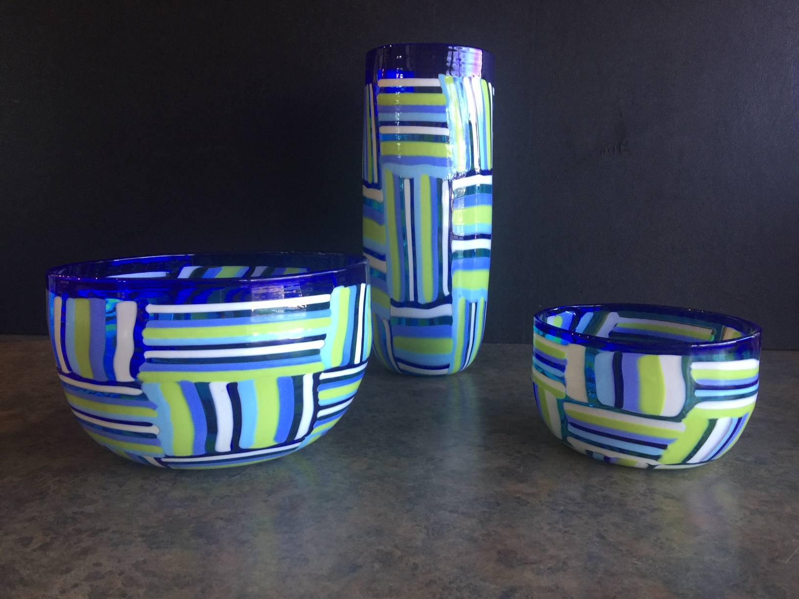 Wonderful collection of two art glass bowls and one vase by Murano Glass. Each piece blends lines of blue, green and white into an eclectic eye-catching piece. Each piece measures: Vase: 11