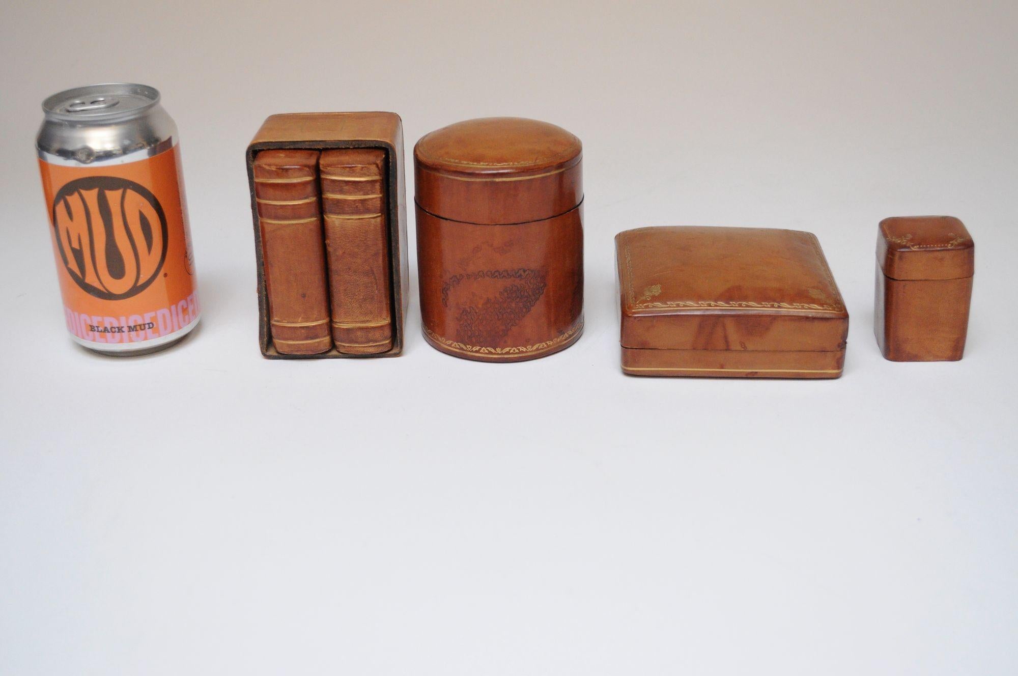 Collection'S di quattro piccole scatole in pelle marrone sfoderate con decorazioni dorate ad intarsio/goffratura di Scuola del Cuoio (ca. anni '70, Firenze, Italia).
Include una tabacchiera cilindrica, una scatola di fiammiferi, una scatola di carte