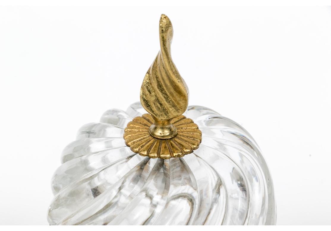 Collectional de trois boîtes en cristal comprenant :
Boîte en cristal avec couvercle en forme de dôme, fleuron en forme de flamme, bande de laiton gaufrée en forme d'œuf et de fléchette, motif tourbillonnant, non marquée, attribuée à Baccarat
