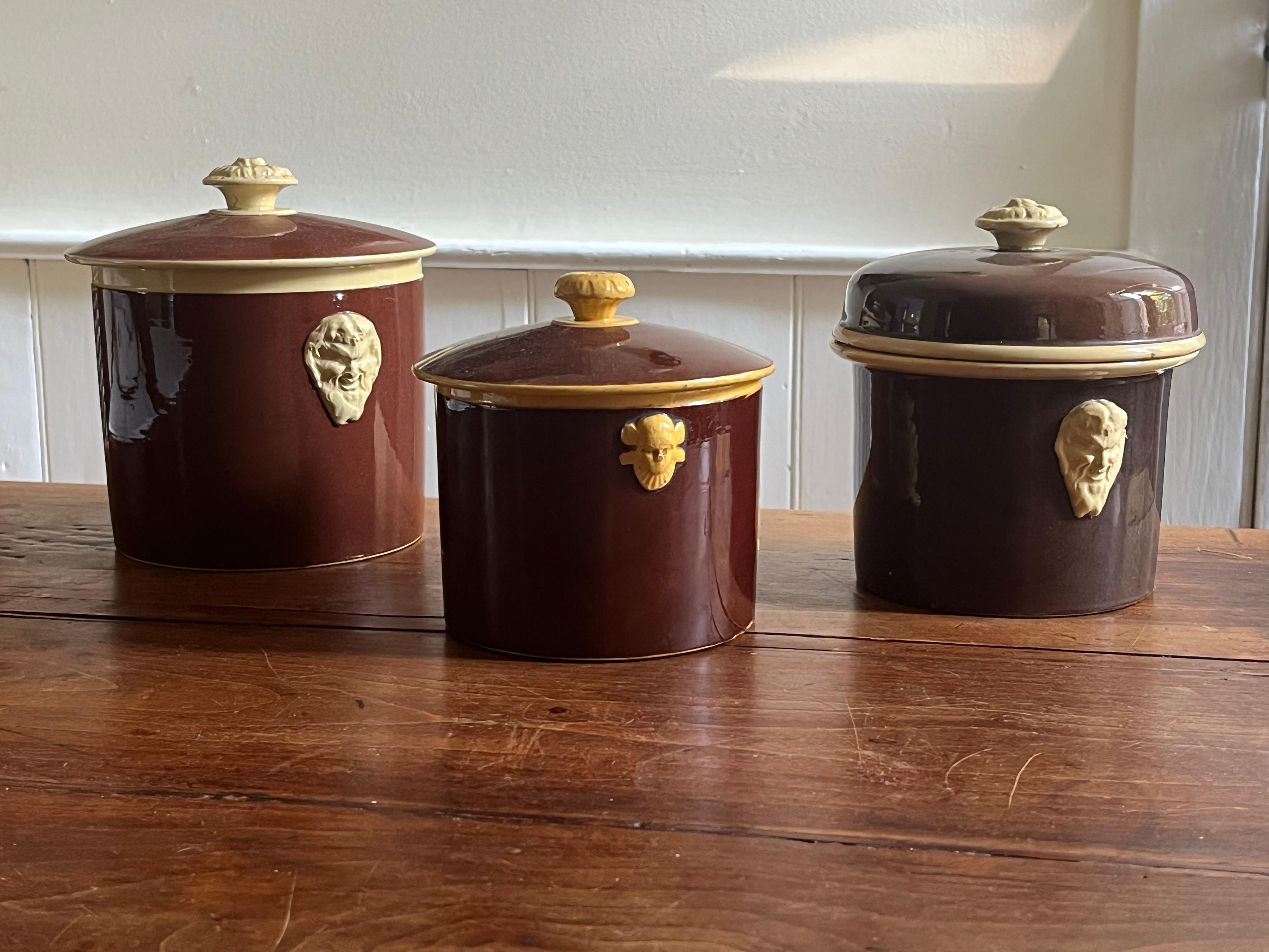 A collection of 3 ceramic pate pots with lids, each with brown glaze and cream colored masks and knobs, French circa 1900. 