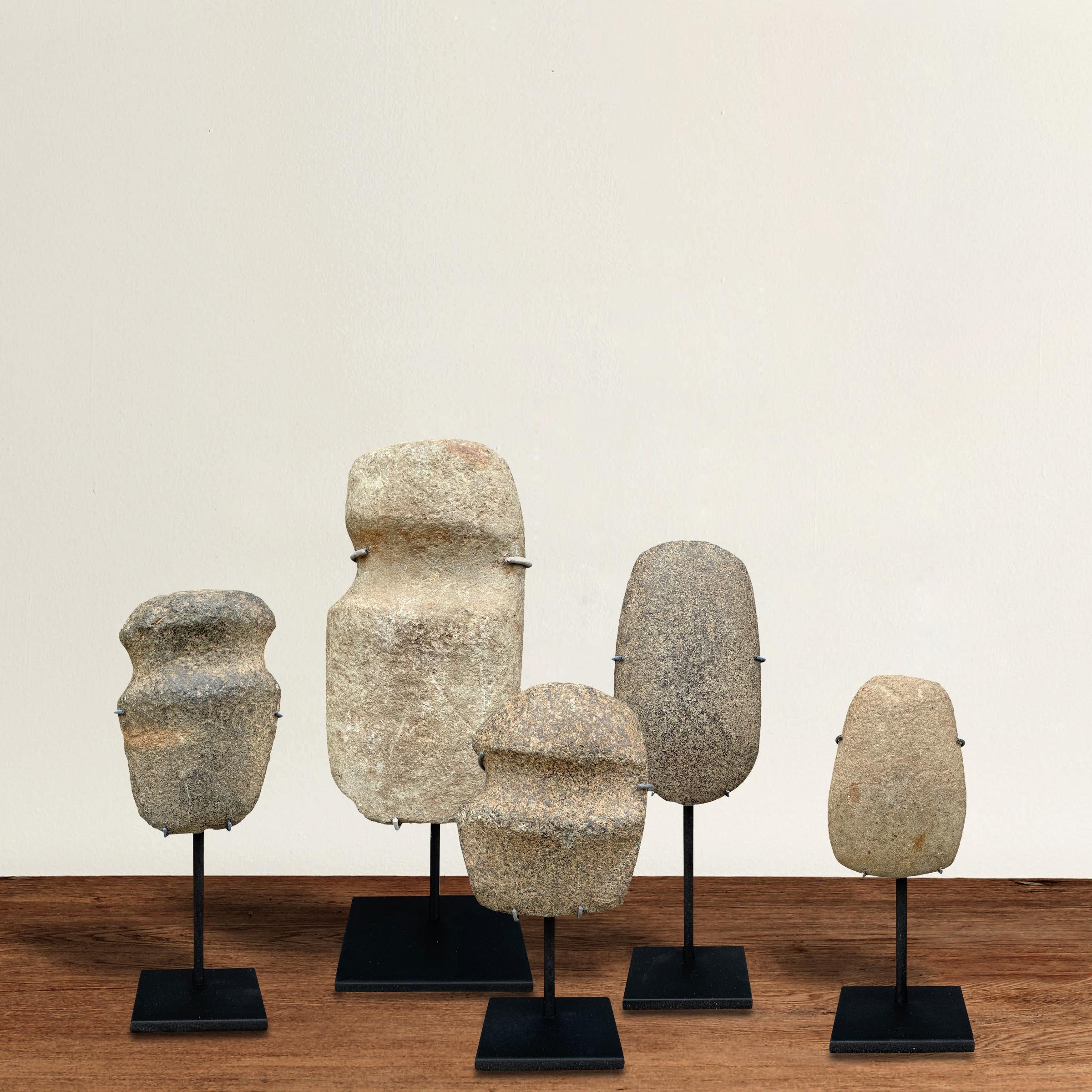 A beautiful stoic collection of Native American Neolithic hand carved stone axe heads with wonderfully sculptural forms, mounted on custom steel stands. Three of the axes have grooves cut into them which helped in tying the heads to wooden handles.