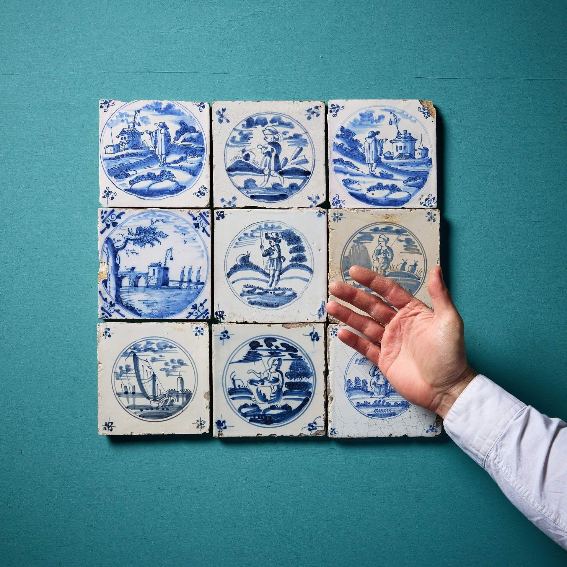 Una collezione di nove antiche piastrelle Delft da 5 pollici che raffigurano scene olandesi con mulini a vento, fanciulle e soldati, tutte in espressiva colorazione blu su sfondo bianco. Ogni immagine offre una meravigliosa illustrazione