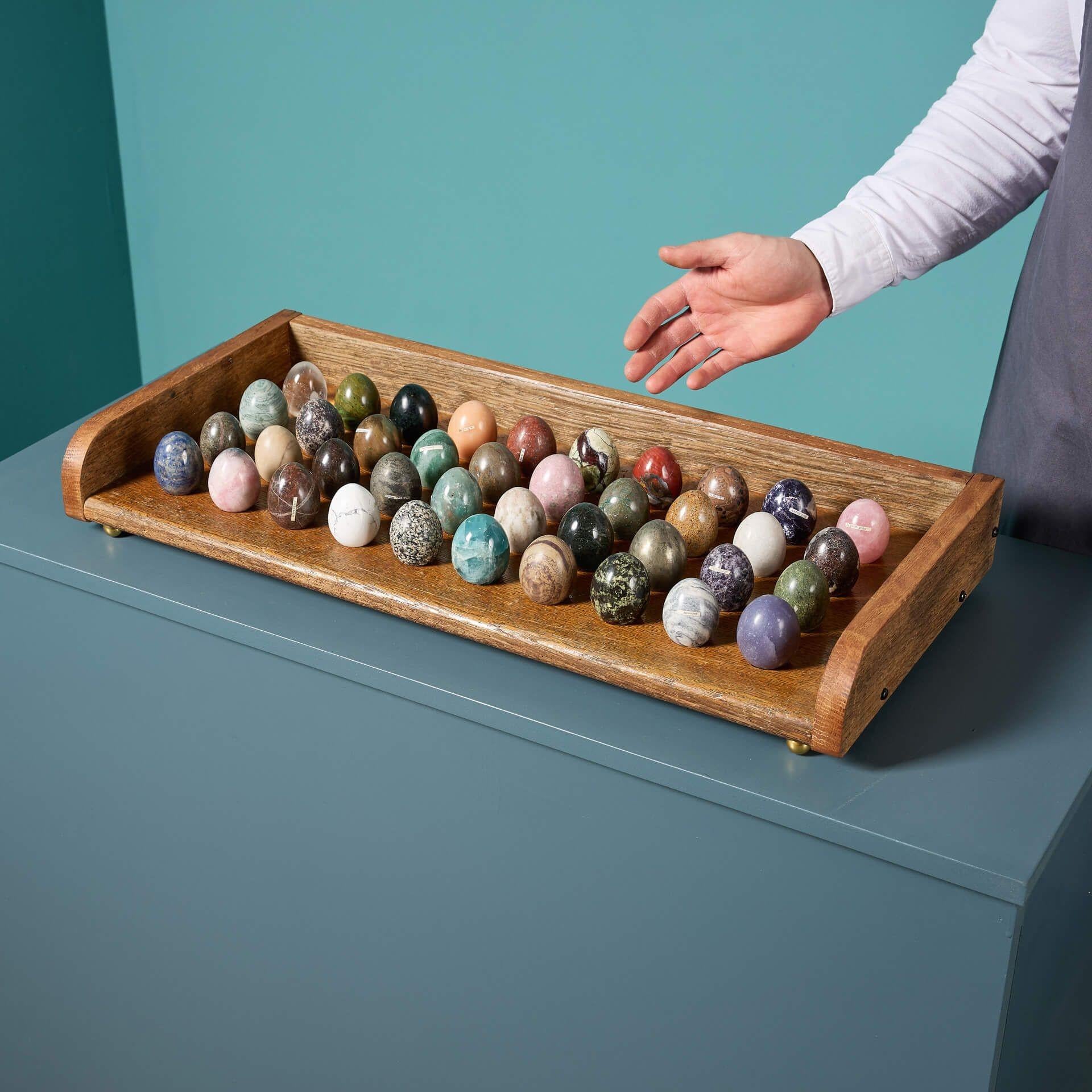 A collection of 40 polished specimen hardstone and marble eggs displaying a variety of minerals.

Displayed in an oak stand with round brass feet, these beautiful eggs include lepidolite, pyrite, calcrete, unakite, serpentine, calcite and optimin in