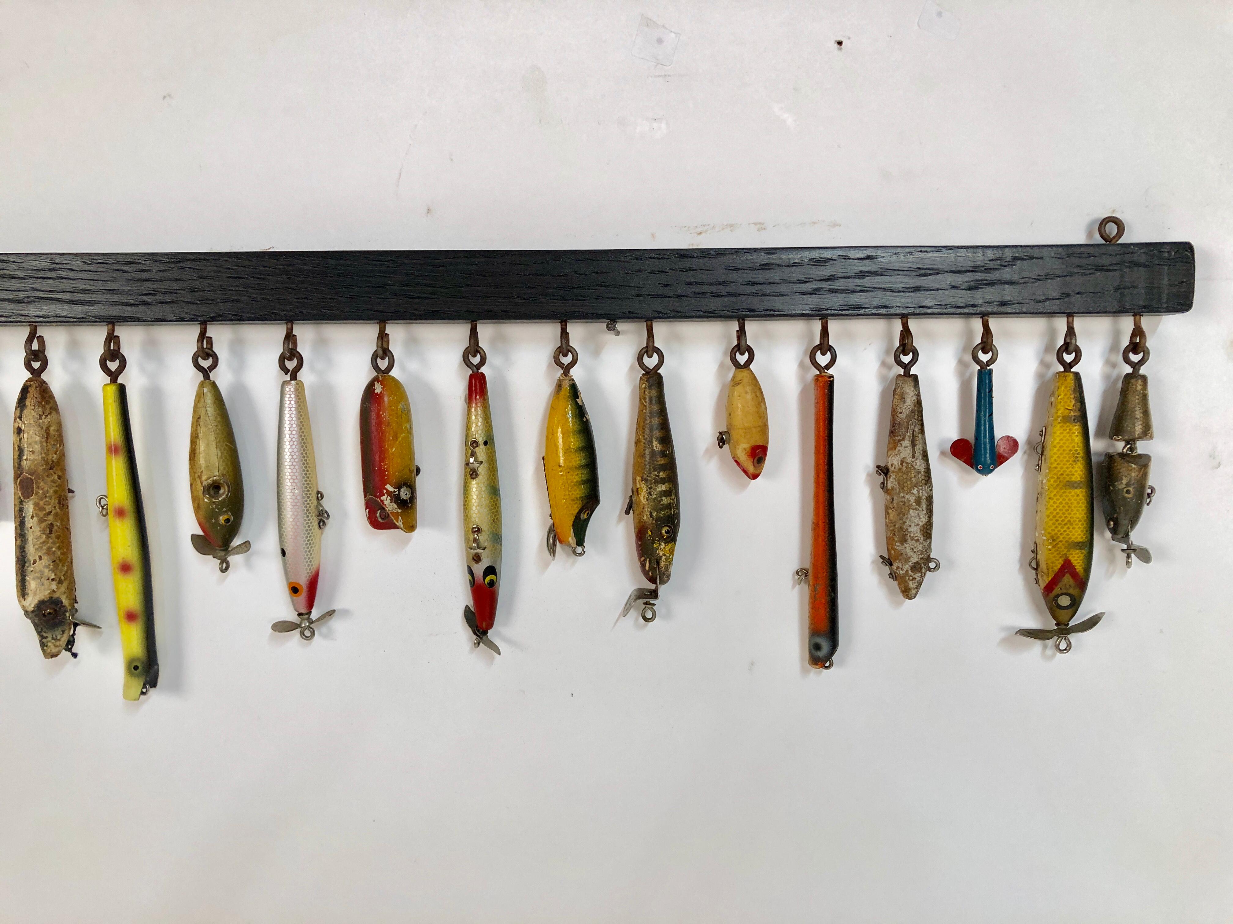 Collection of thirty antique wooden fishing lures custom mounted on black painted oak with acid screws, circa 1940-1950.