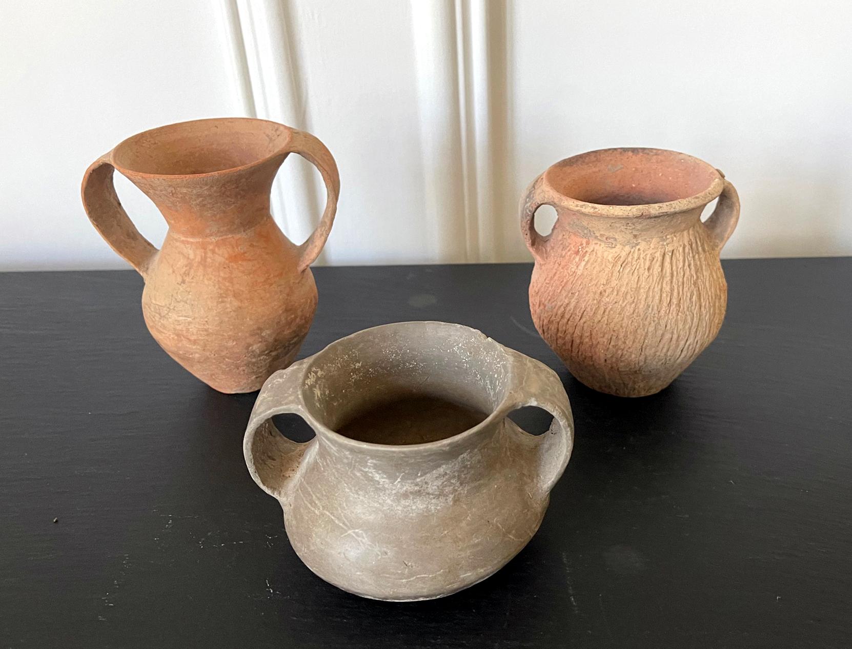 A collection of three small Chinese Neolithic pottery jars consisting a red slender jar with large double ears, a grey and wide short jar with double ears and a more stocky jar with thick wall and engrave-decorated surface. They are all low fired