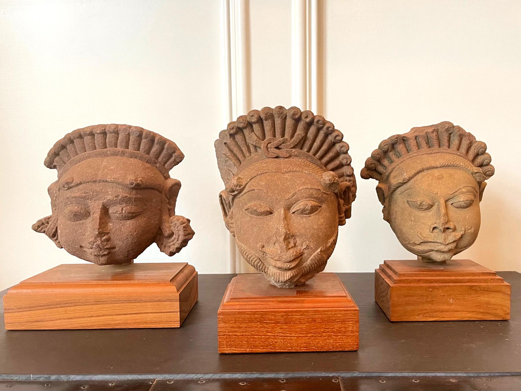 Collection de trois têtes sculptées en grès sur des présentoirs en bois provenant du nord de l'Inde, du Rajasthan ou de l'Inde. 
 Madhya Pradesh, vers 11-12e siècle. Fragmentées d'une grande statue au corps entier, ces têtes en grès rouge