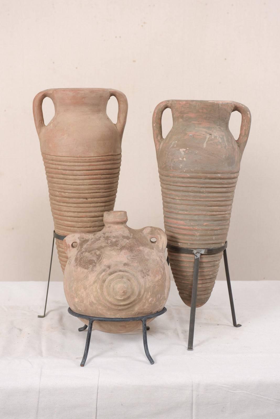 A collection of three Mediterranean terracotta jars on custom stands. These vintage terracotta vessels make for a lovely decorative collection, the two taller ones having nicely ribbed and oblong bodies that taper to a point at their bottoms, the