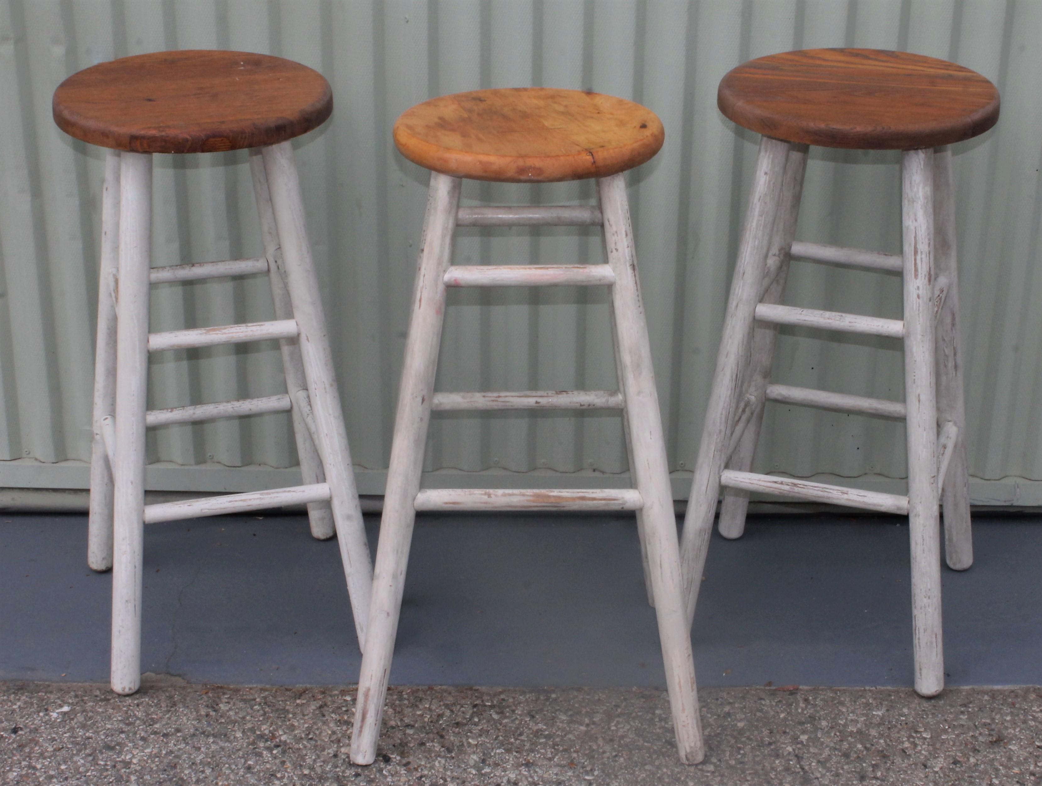 This collection of three white painted pine bar stools have original oak seats and are in very sturdy condition. There is a pair of matching and one added to the pair.