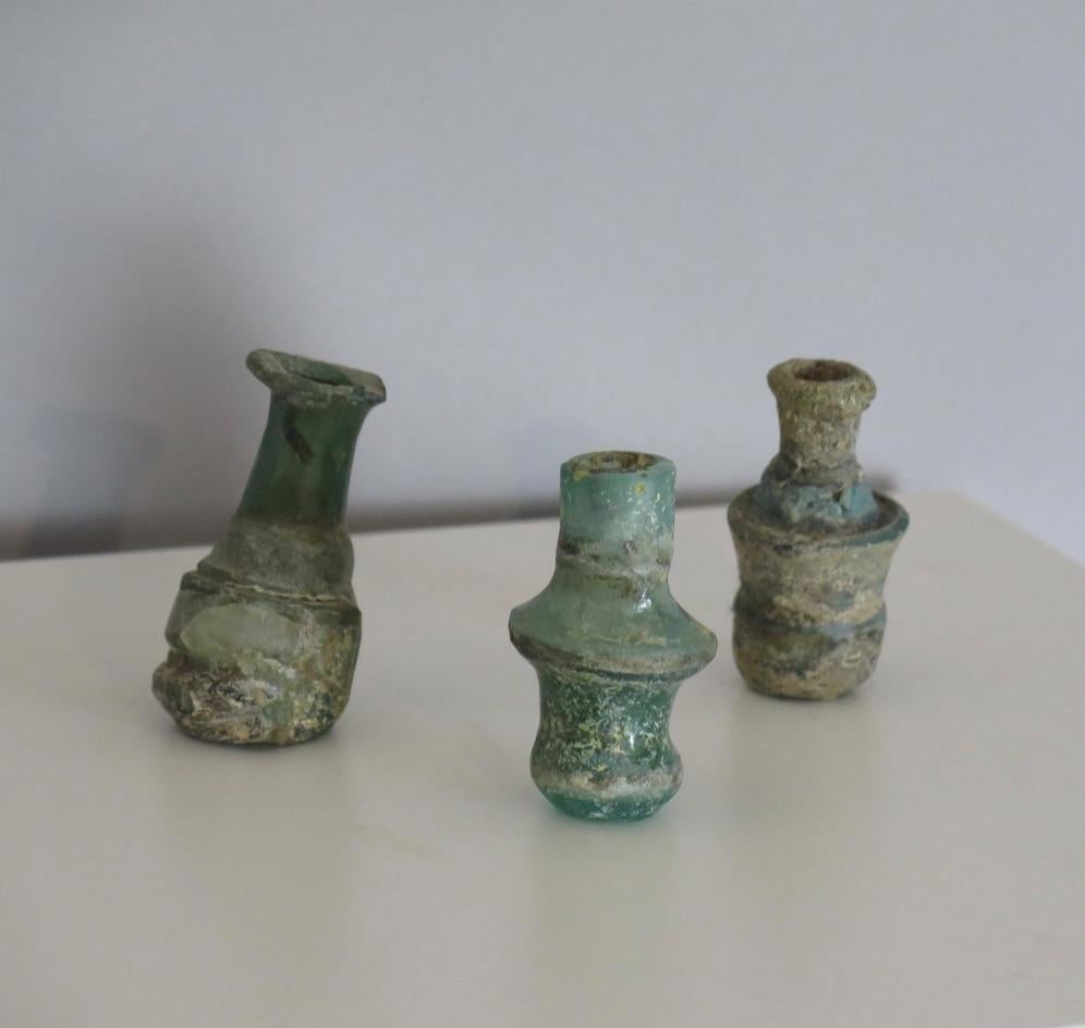 Collection of Three Ancient, Heavily Patinated Iridescent Roman Glass Bottles. 
Dimensions vary from 2-4” H and 1-2” Diameter. 

