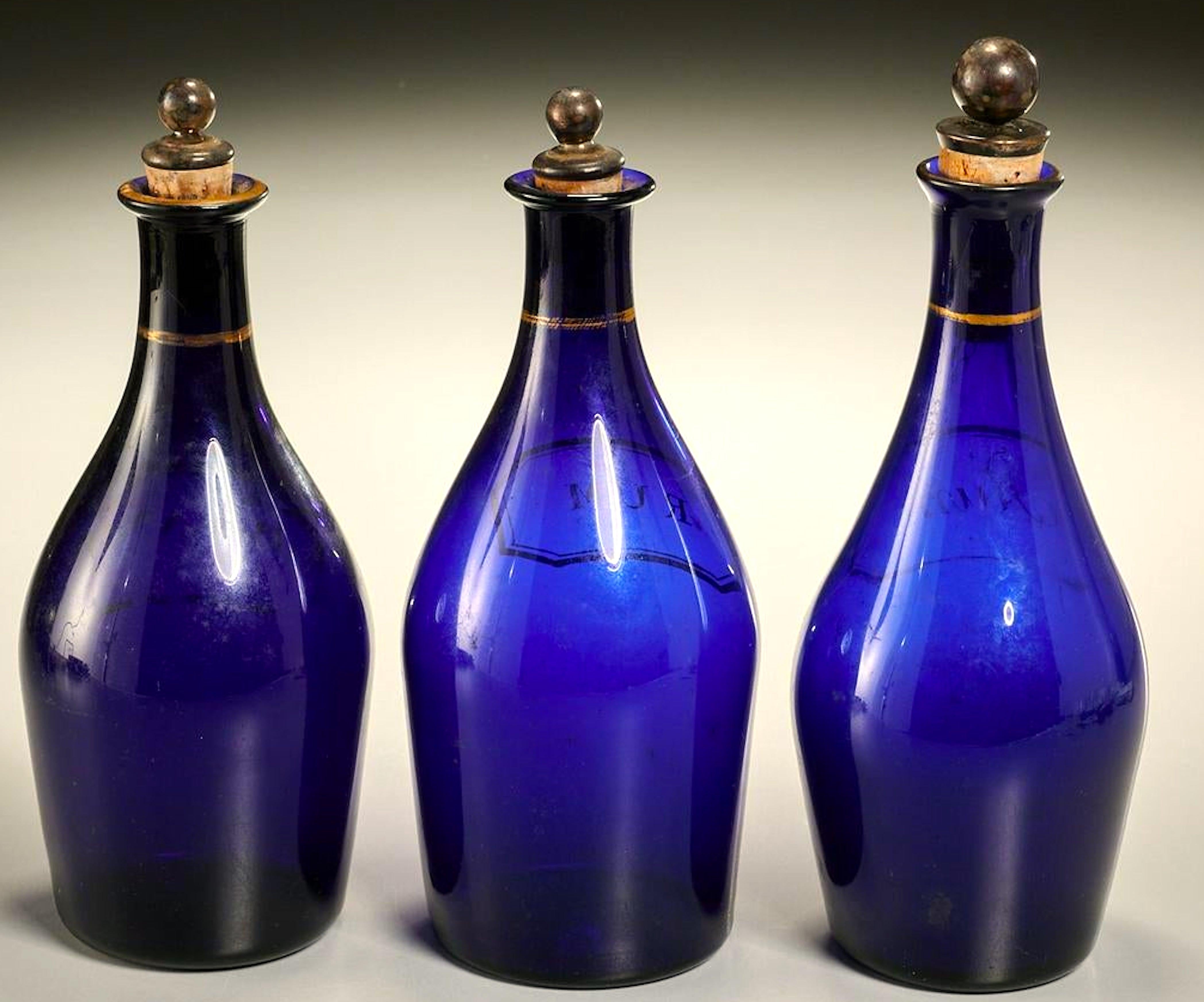 Rares bouteilles en bleu de cobalt de George III, vers 1820. Trois au total, Rhum, Rhum et Brandy. En très bon état pour leur âge, chacun avec un bouchon en argent et en liège et des lettres et décorations dorées. Chacune mesure environ 9