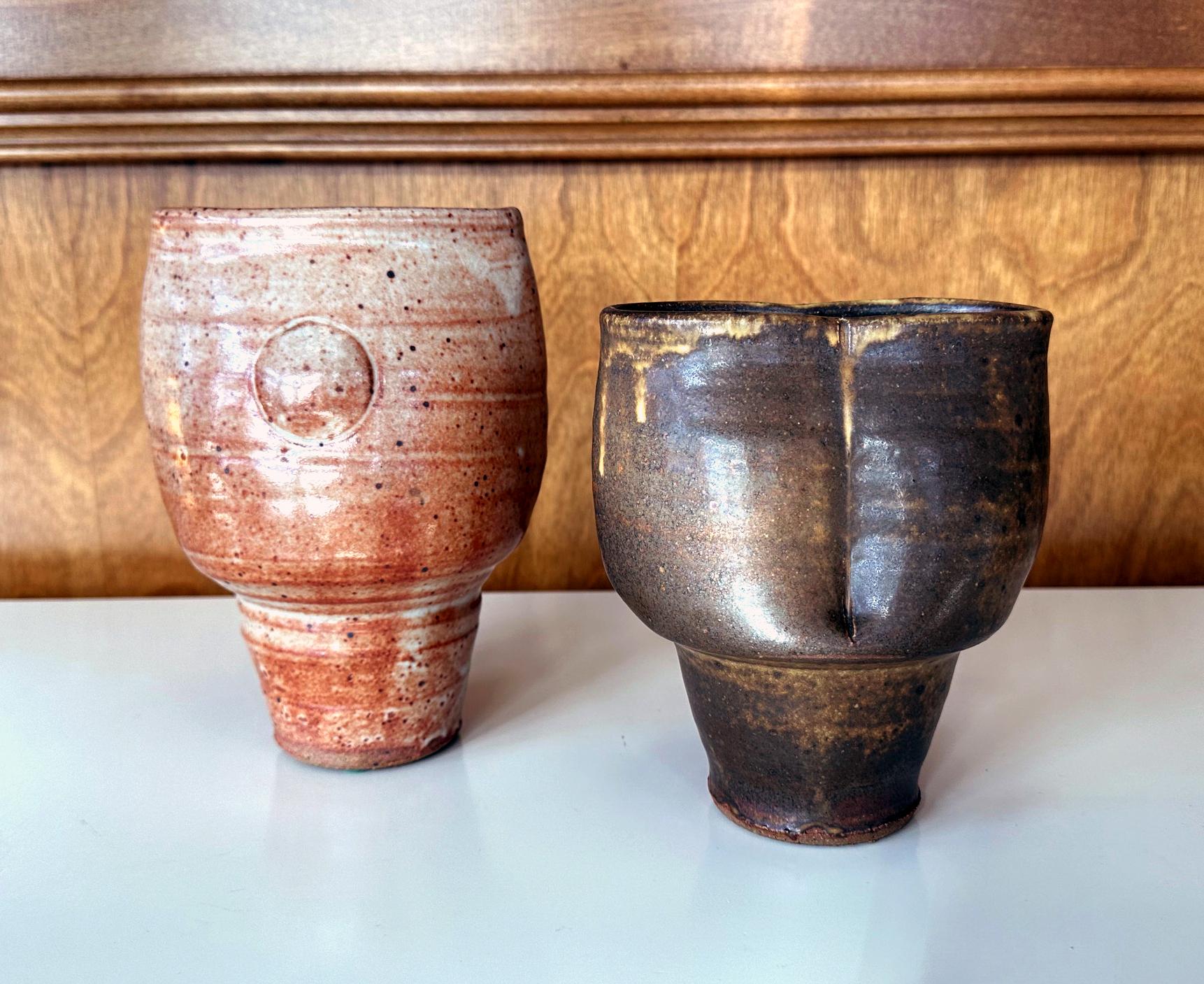 An assemble of two stemmed cylinder-shape stoneware vases by American studio potter Warren MacKenzie (1924-2018). The two vases have a complementary form and silouette and display nicely together. The surface of the slightly taller vase is covered